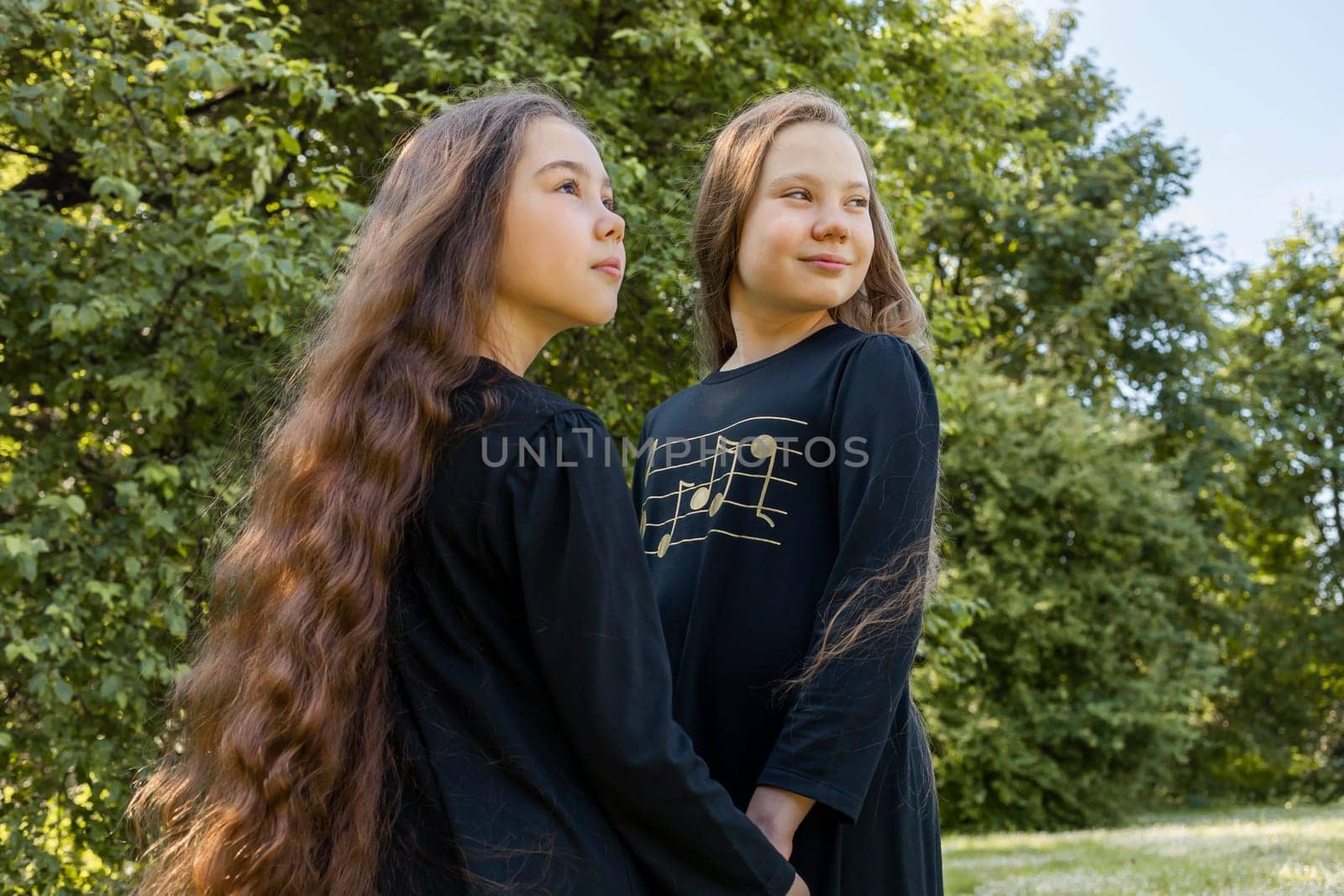 Two Little Girls, Sisters With Extra Long Curly Shiny Hair Hold Hands In Park, Nature On Background. Outdoor, Sunny Day. Cute Happy Kids In Dress Walking In Meadow. Siblings. Horizontal Plane.