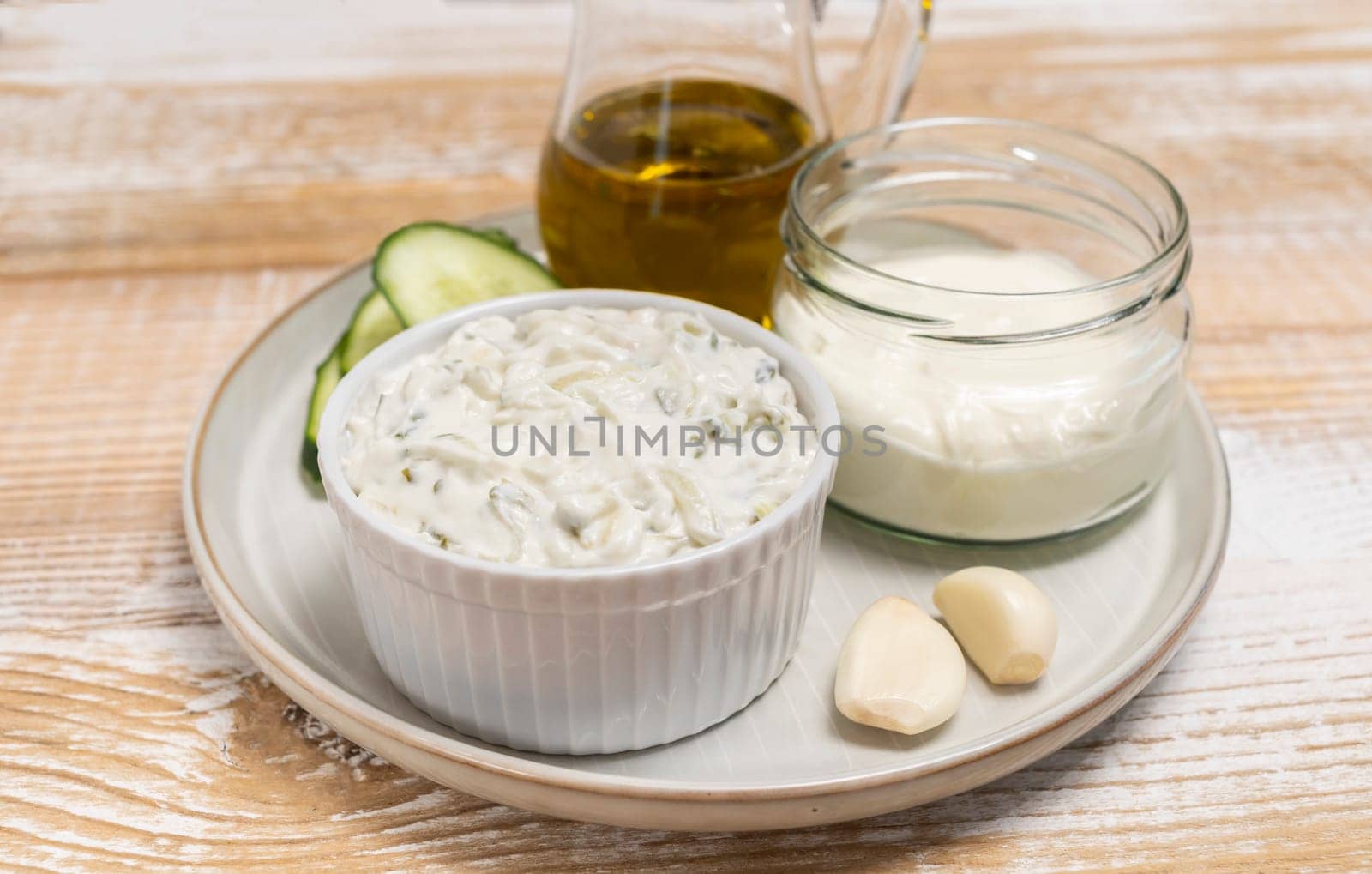 Traditional greek yogurt sauce Tzatziki in white bowl, made of chopped cucumbers, sour cream yogurt,olive oil,garlic,herbs with ingredients on wooden table. Rustic style. Close up, horizontal plane.