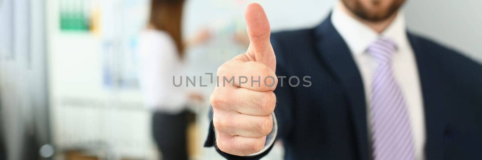 Businessman showing thumb up sign of success over blurred team of business people by kuprevich