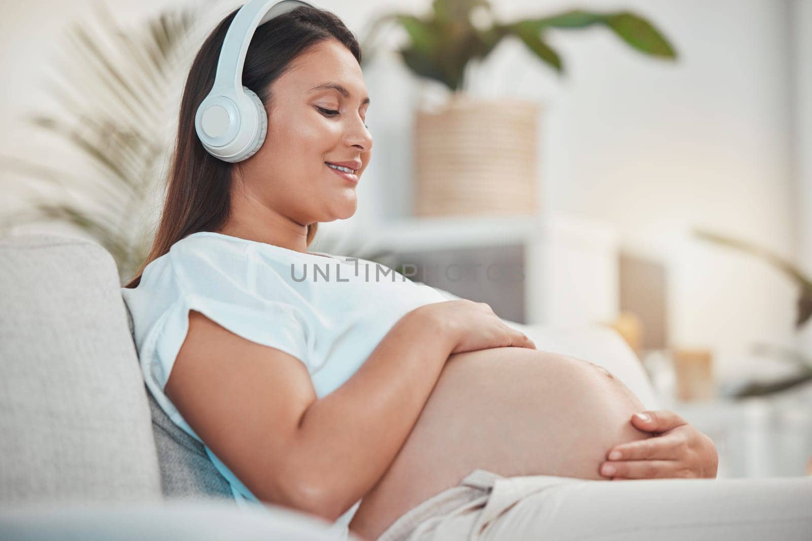 Pregnant woman, music and holding belly or bump while relaxing and bonding with her baby at home. Babies, mother touching stomach and listen to audio on headset for bond in family home by YuriArcurs