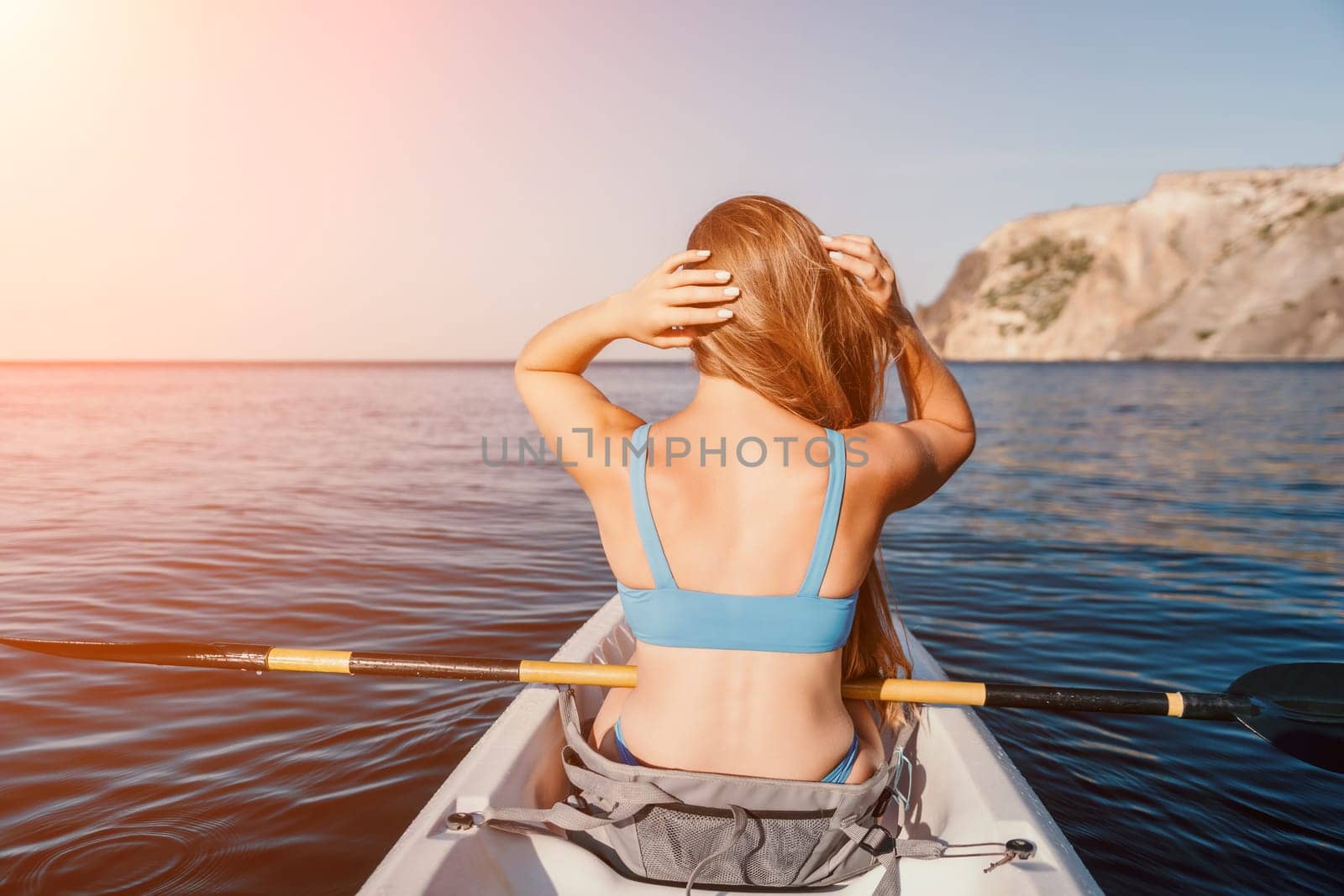 Woman in kayak back view. Happy young woman with long hair floating in transparent kayak on the crystal clear sea. Summer holiday vacation and cheerful female people relaxing having fun on the boat