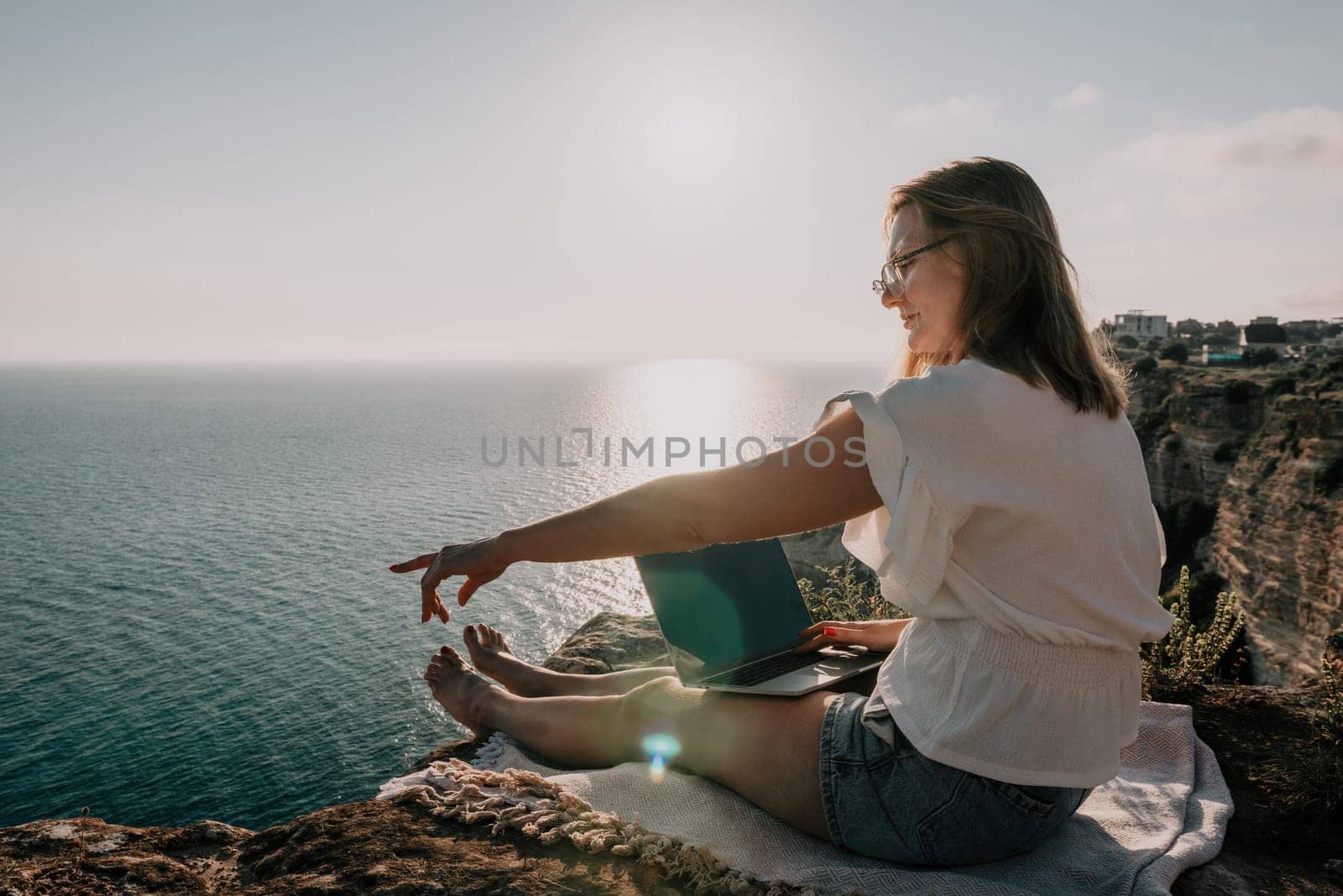 Woman sea laptop. Business woman in yellow hat working on laptop by sea. Close up on hands of pretty lady typing on computer outdoors summer day. Freelance, digital nomad, travel and holidays concept.