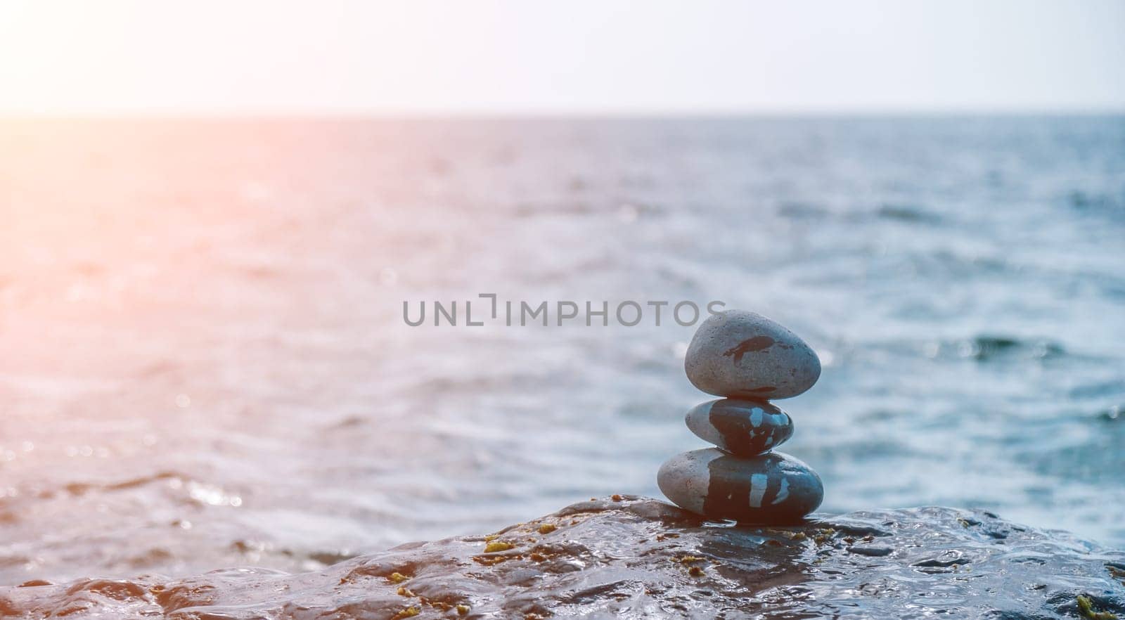 Balanced Pebbles Pyramid on the Beach on Sunny Day and Clear Sky at Sunset. Blue Sea on Background Selective focus, zen stones on sea beach, meditation, spa, harmony, calm, balance concept.