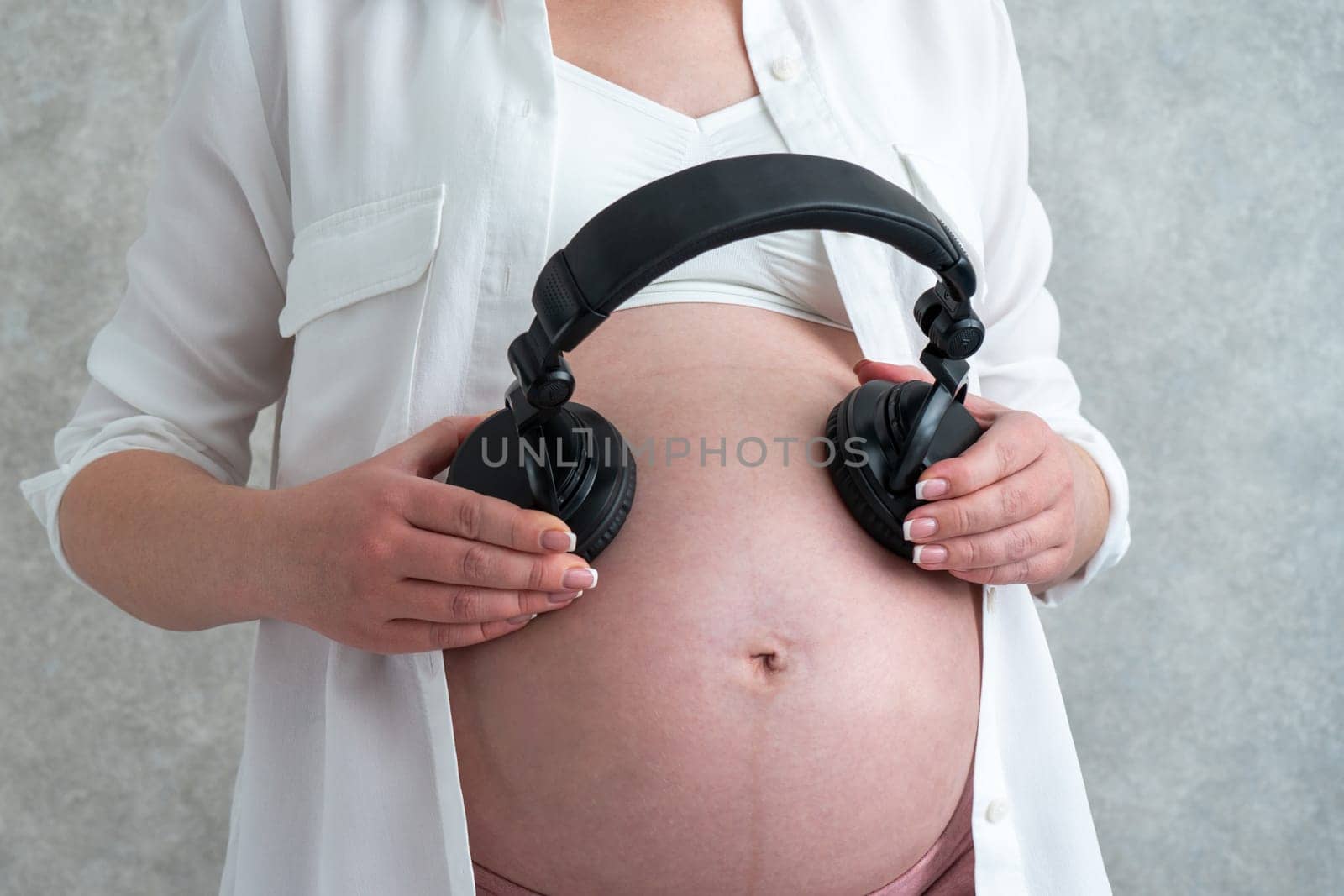 Pregnant woman playing music to her baby through headphones putting them on her belly by Mariakray