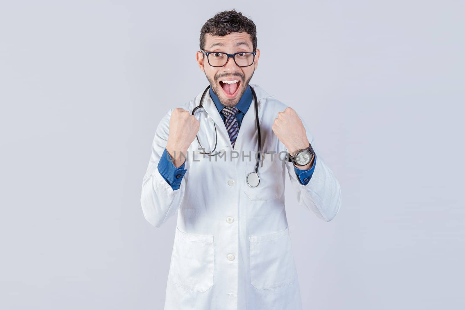 Young doctor is happy celebrating something, he is wearing glasses and stethoscope, he is looking at the camera with amazed face