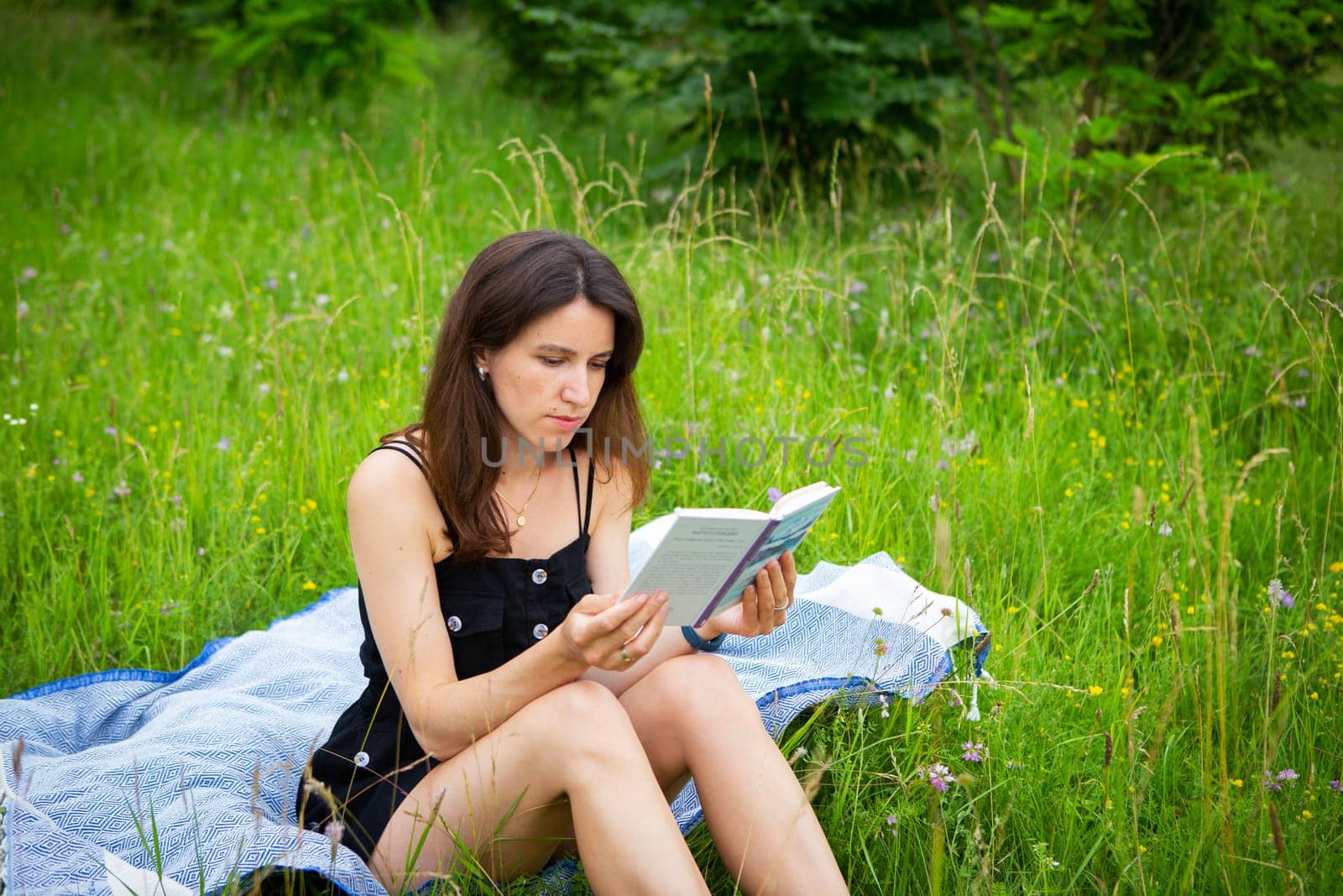 Outdoor picnic. A girl reads a book in the open air while sitting on a blue plaid. The girl enjoys the fresh air. Outdoor recreation