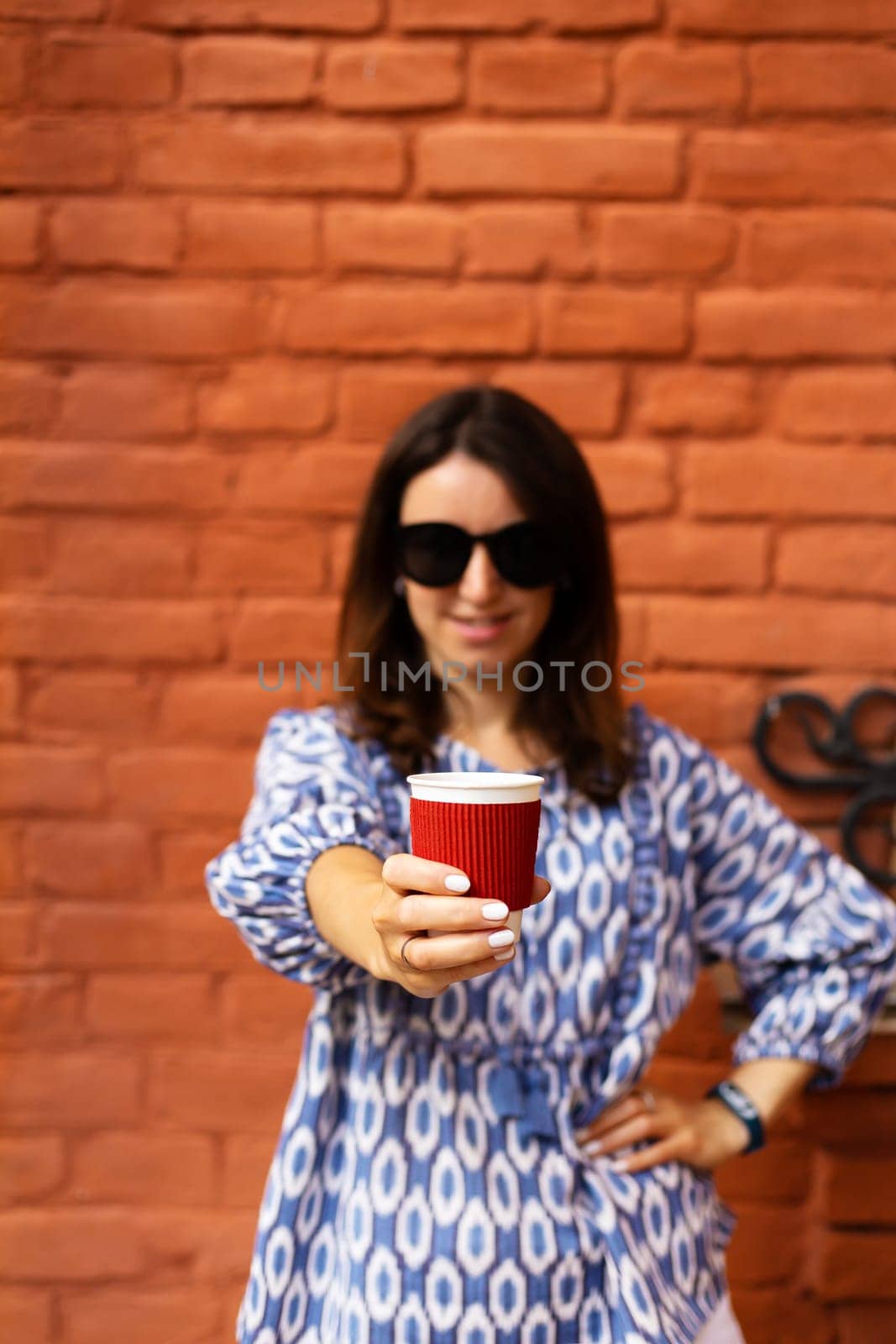 Portrait of a young beautiful woman holding a plastic red glass with coffee in front of her