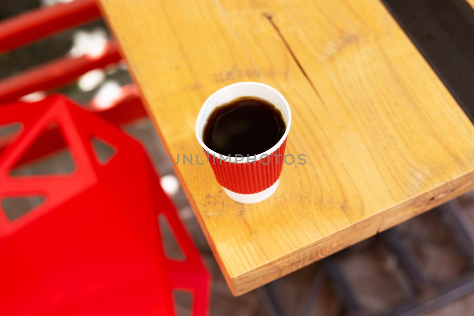 A wooden table on which there is a red plastic cup with coffee. Summer beautiful terrace in greenery. Cozy place
