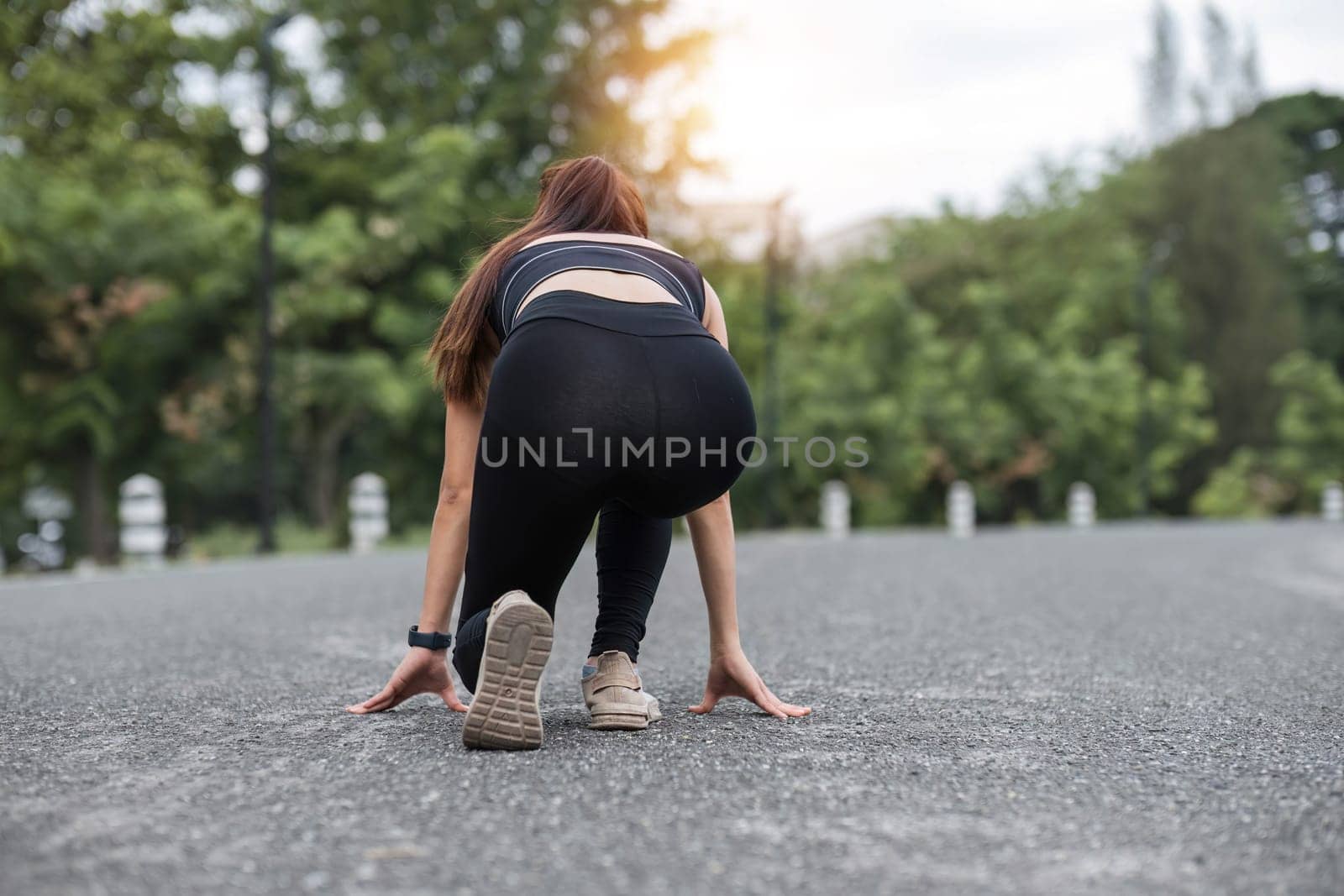 Athlete Asian female runner in comfortable sportswear in running start pose, preparing to run on the street. active lifestyle concept, back view by wichayada