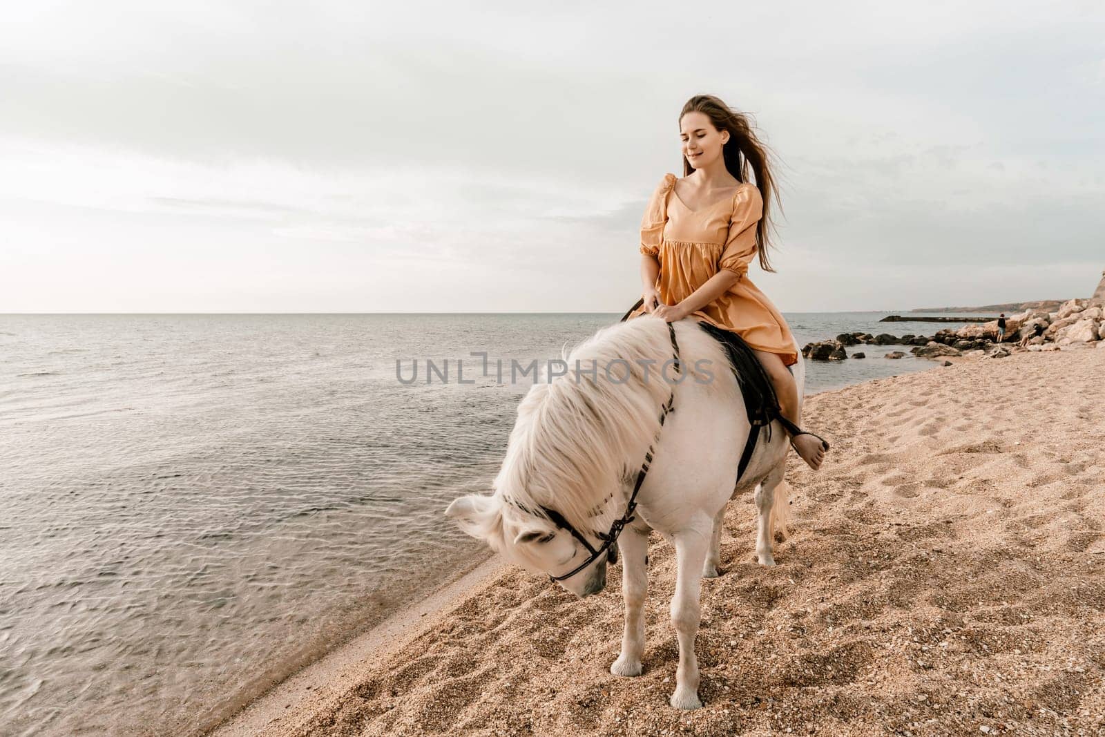 A white horse and a woman in a dress stand on a beach, with the sky and sea creating a picturesque backdrop for the scene