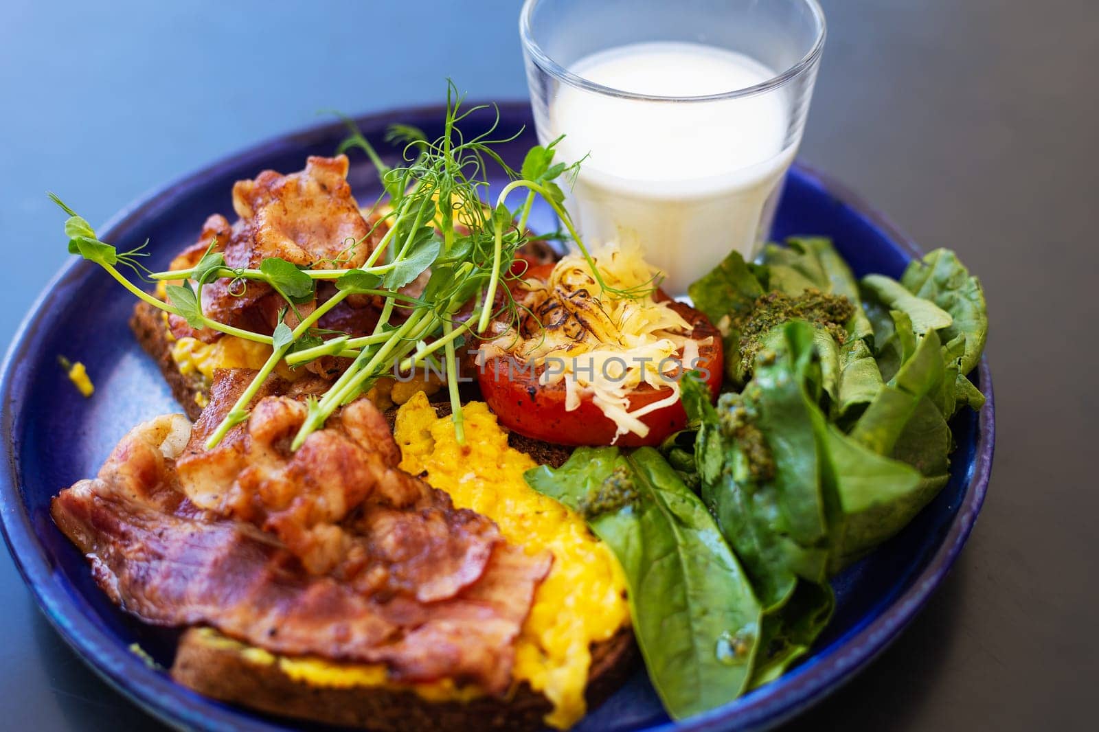 Very bright and healthy breakfast on a plate - bacon, egg, salad, tomato, cheese, a glass of yogurt. Close-up
