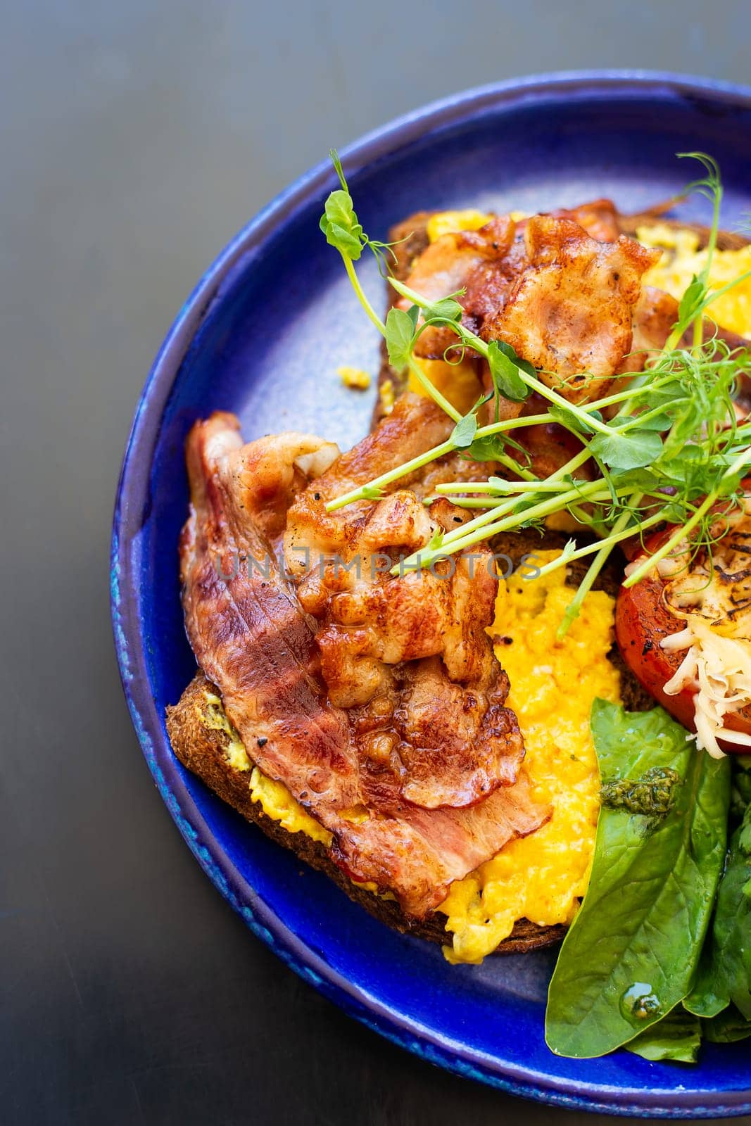 Very bright and healthy breakfast on a plate - bacon, egg, salad, tomato, cheese, a glass of yogurt. Close-up, top view