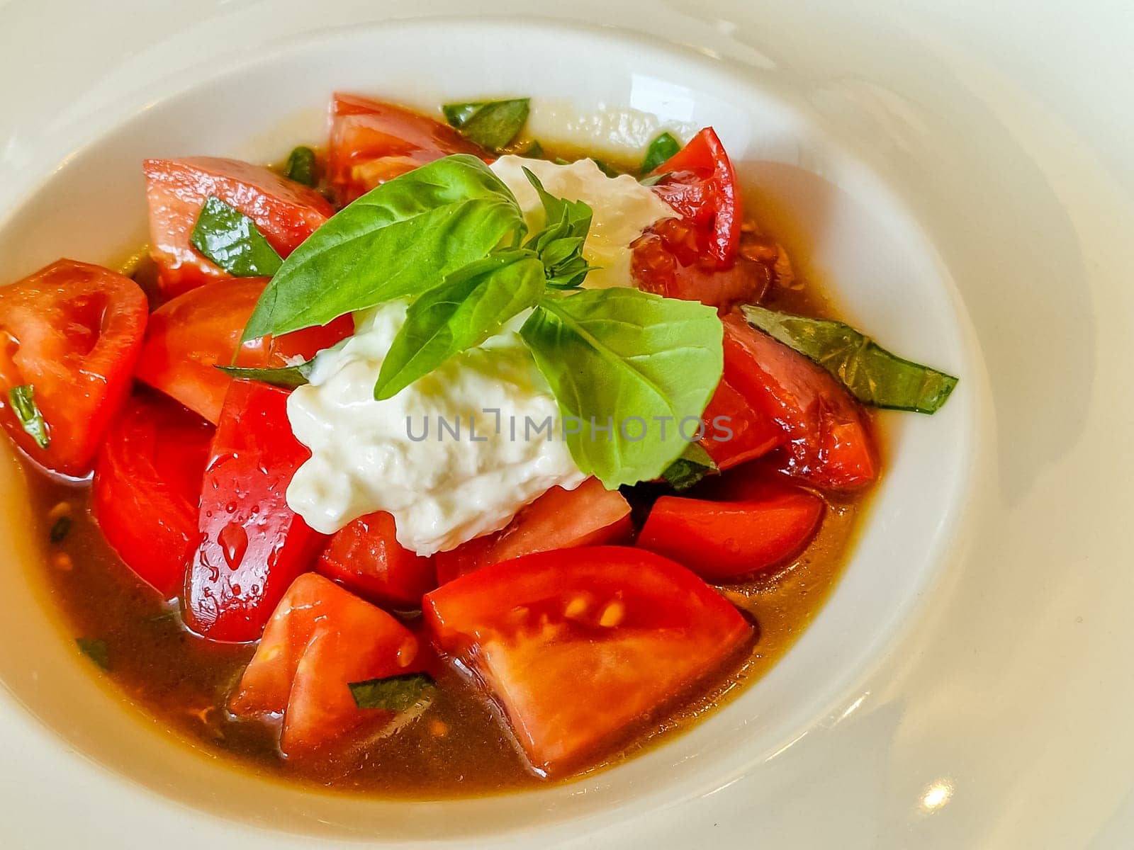 Sliced fresh Italian burrata cheese with tomato slices on a white plate on a white background.