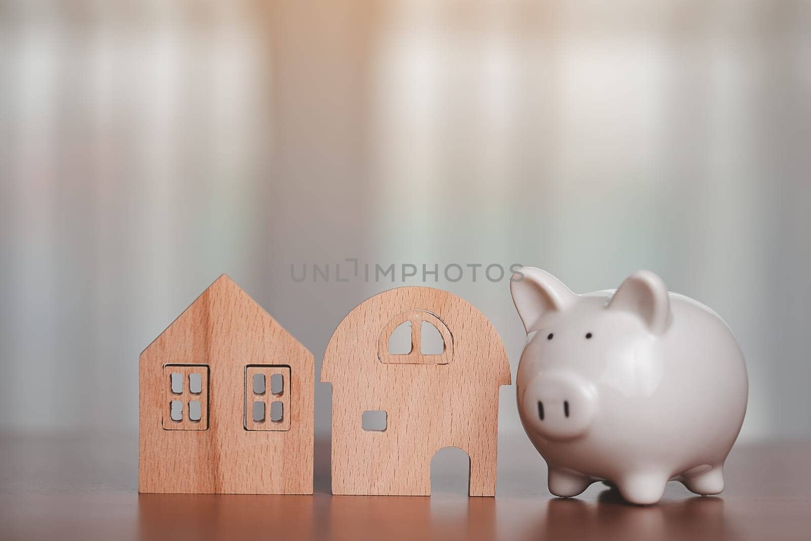 Saving piggy bank with wooden house model on the table for business, finance, saving money and property investment concept.