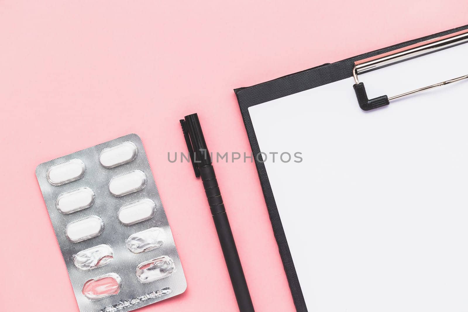 Top view of clipboard with paper, black pen and blister pack of medicine pill on pink background for medical and healthcare concept