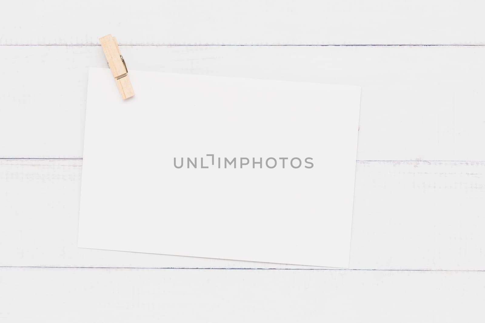 Blank white paper card with wooden clamp on white table background for wedding invitation card design and writing or printing on.