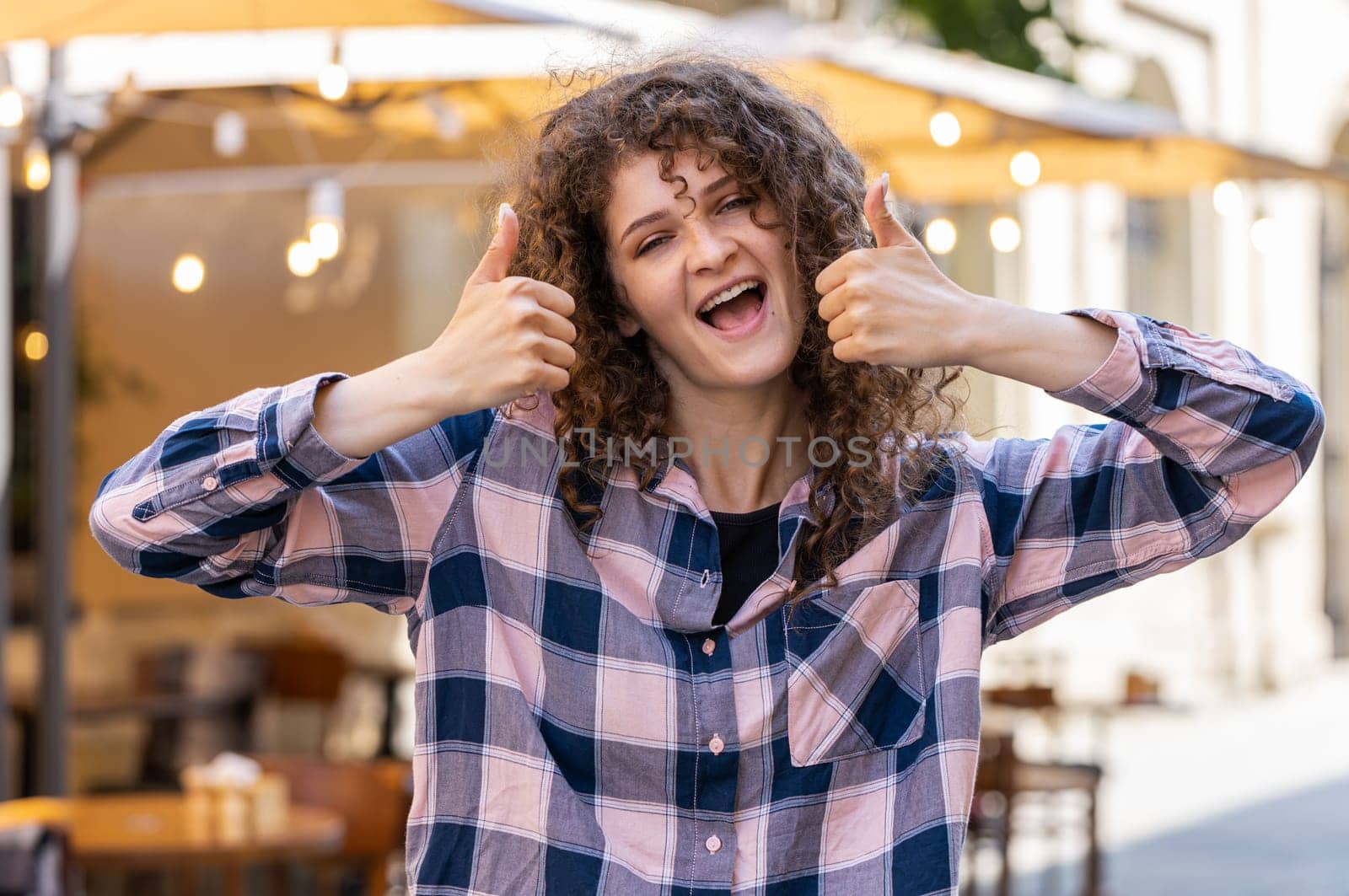 Like. Happy pretty young woman looking approvingly at camera showing thumbs up, like sign positive something good positive feedback. Girl walking in urban city sunshine street. Town lifestyles outdoor