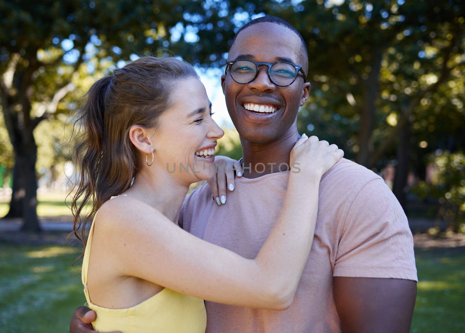 Summer, love and laugh with an interracial couple hugging outdoor together in a park or garden. Nature, diversity and romance with a man and woman bonding while on a date outside in the countryside.