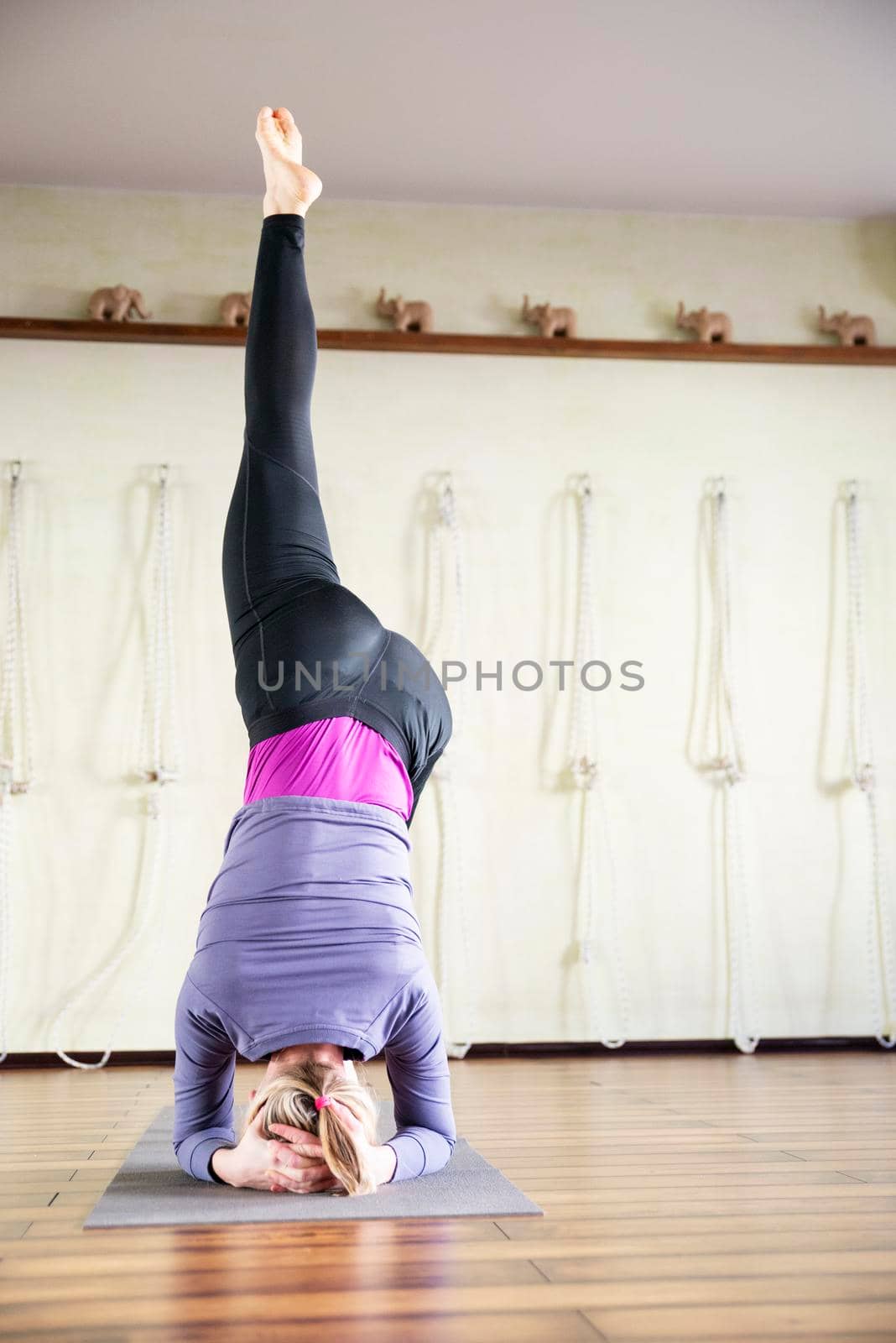 woman having yoga practice and standing on head. Concept of physical and mental health, happy living and well being. by Mariakray