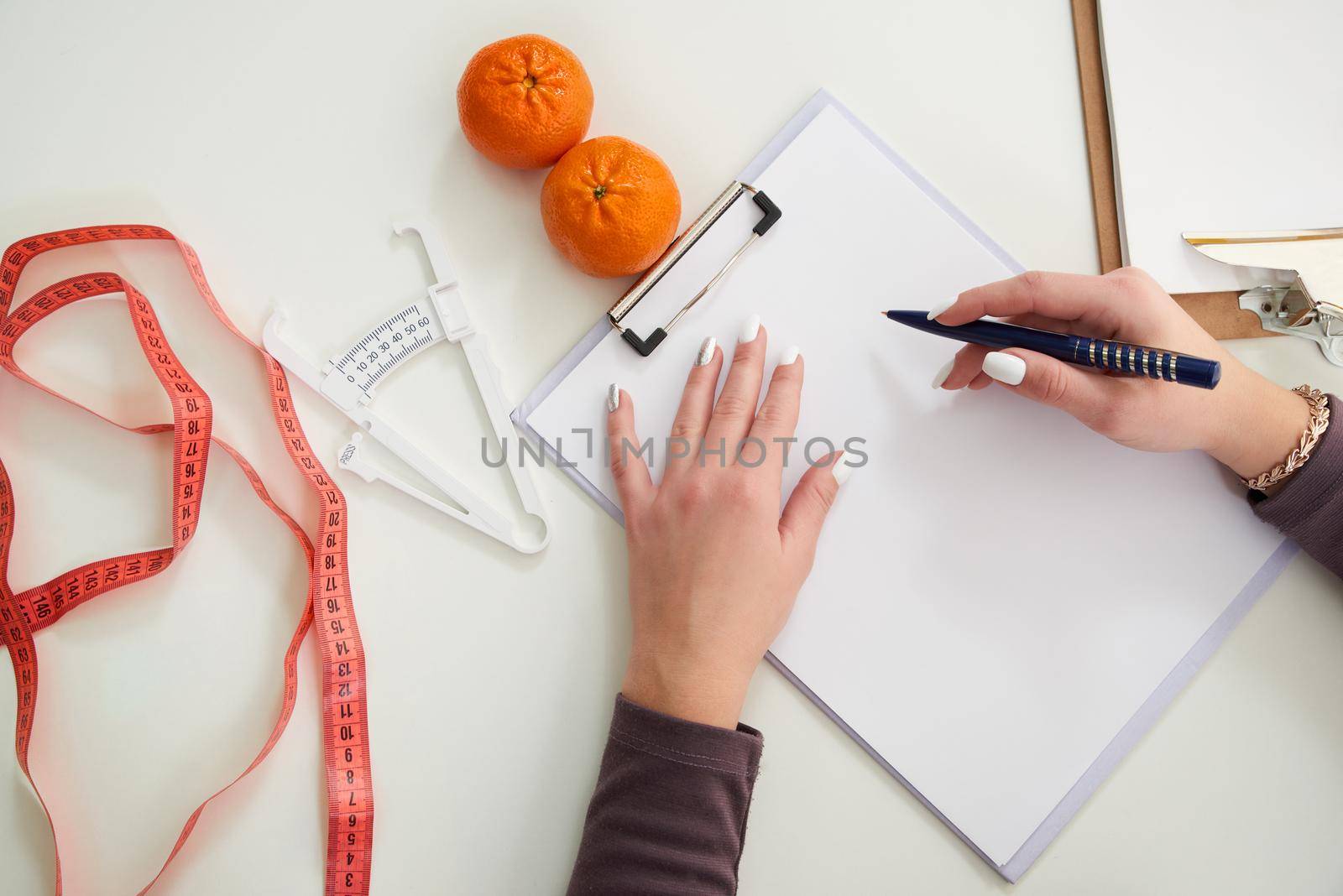 Nutritionist doctor writing diet plan on table with measuring tape, top view