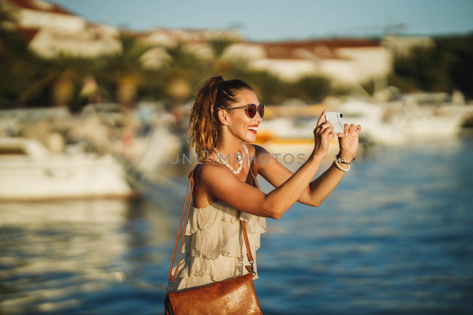 Shot of a young woman taking photos with her smartphone while exploring the wonderful seaside of Meditteranian.