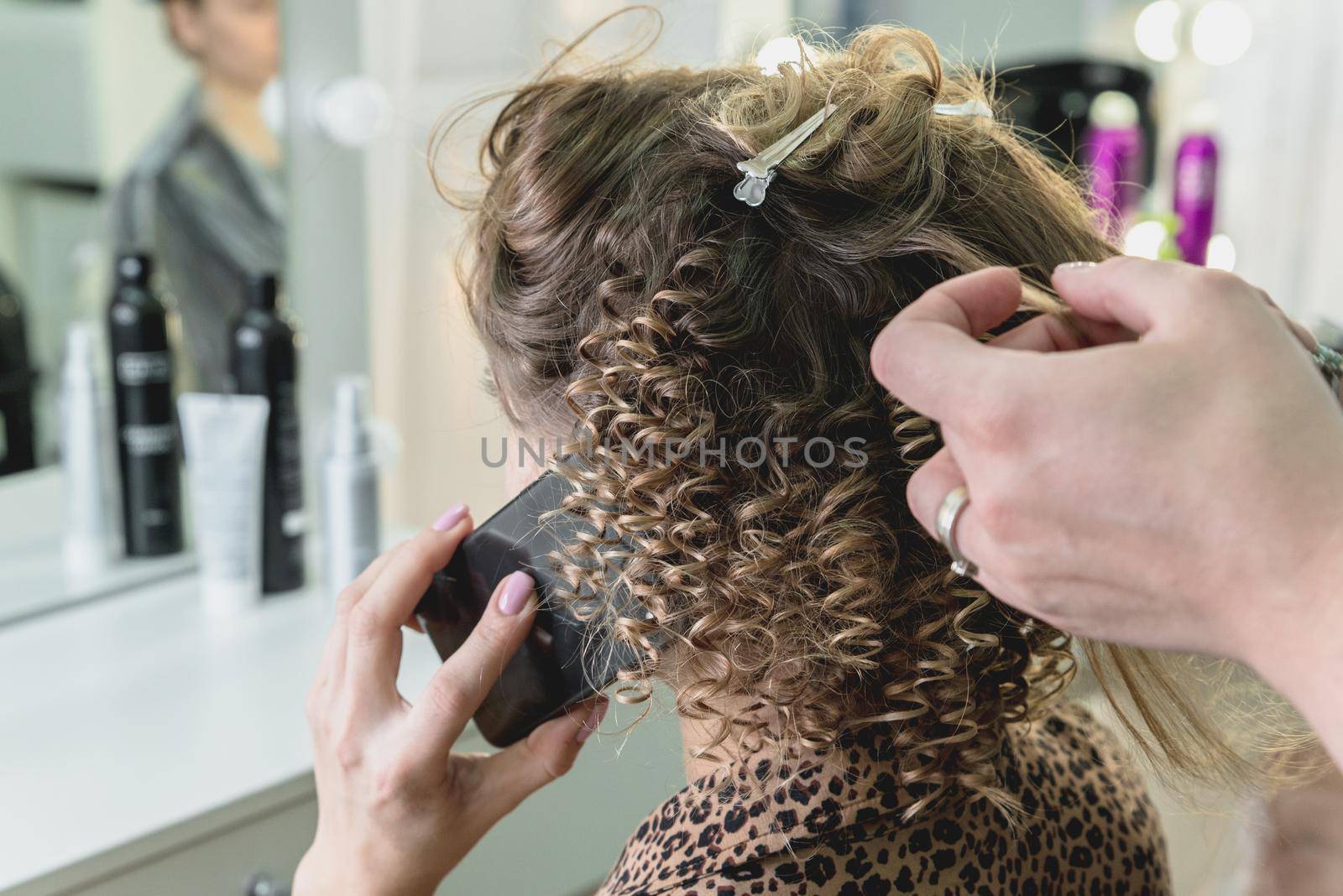 Hairdresser working with beautiful woman brown hair in hairdressing salon. Close up view of hand, curling iron and the appliance