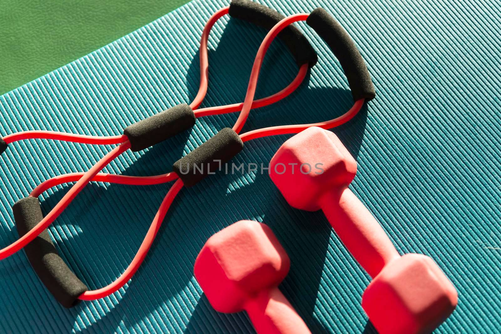 Top view of mat placed on wooden floor with bottle of water and smartphone near rubber expander in fitness club