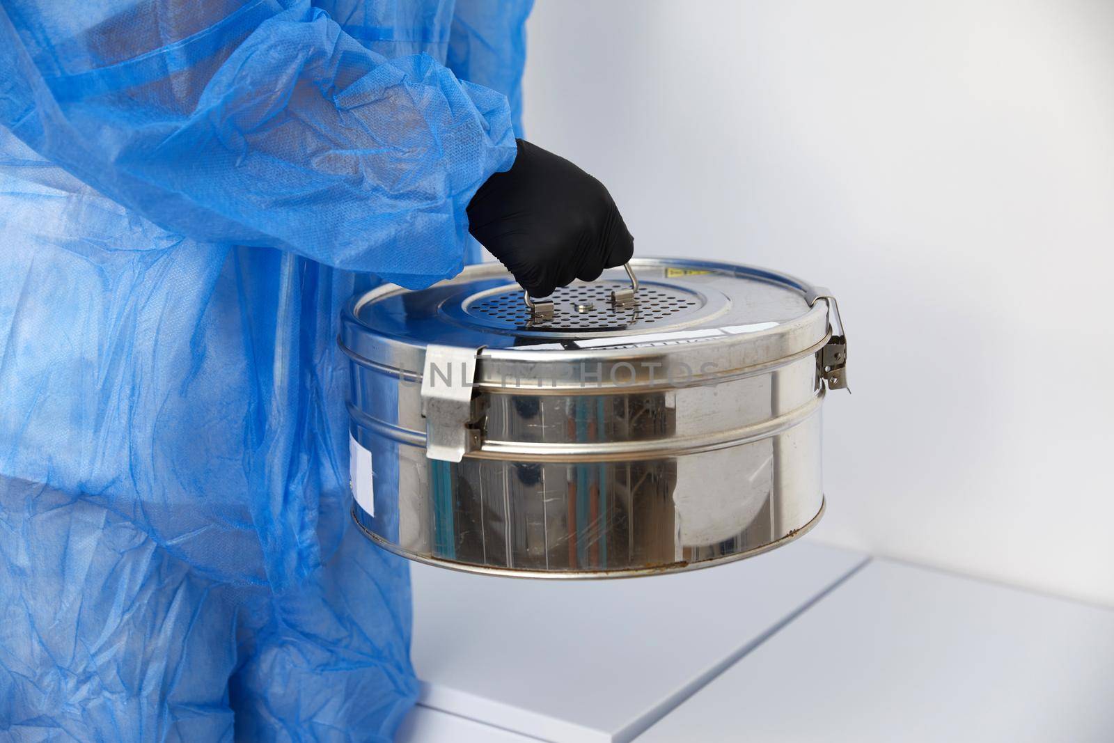 A Person standing in Laboratory holding Autoclave Sterilizer metal box wearing protective uniform
