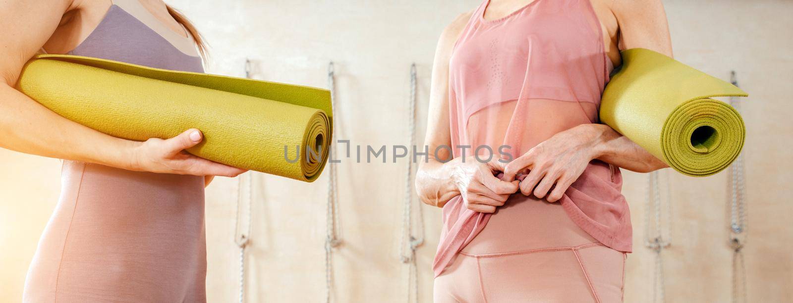 Woman wearing activewear standing in gym holding yoga mat ready start fitness or yoga training. Concept of sports lifestyle. Yoga concept