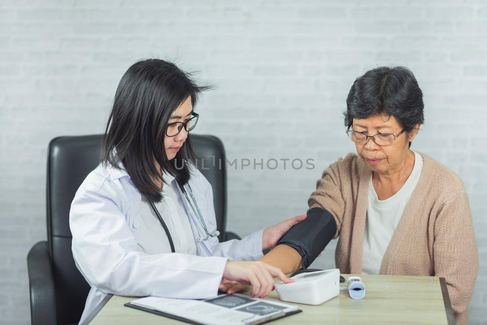 doctor checking pressure old woman on gray background by Wmpix