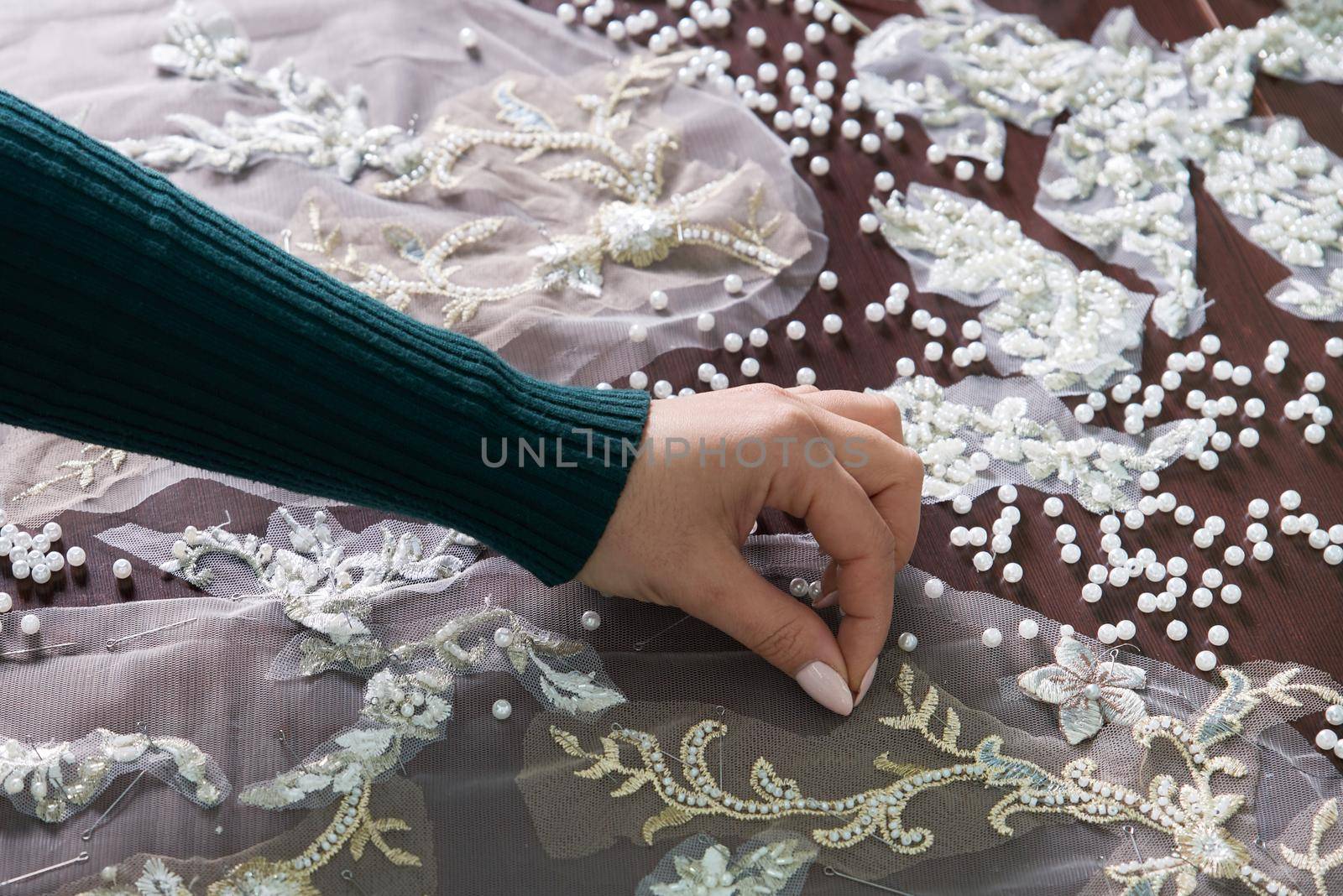 close-up of female hands of seamstress tailor sewing wedding dress using beads and lace in the studio