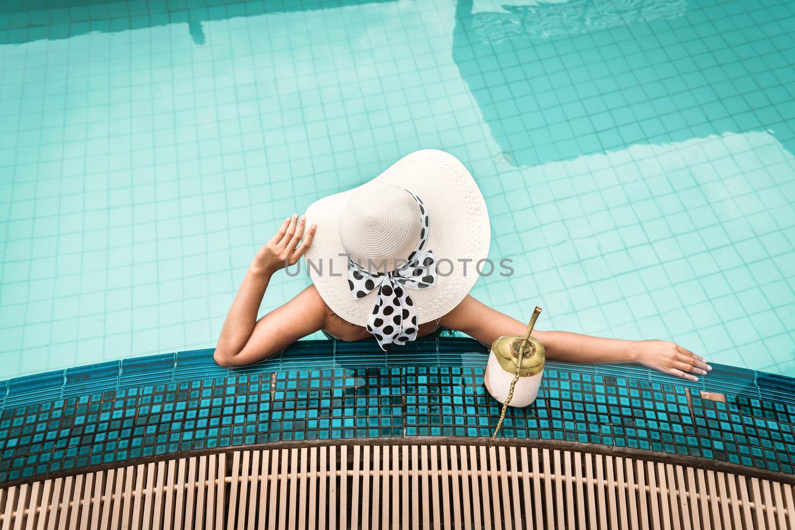 Sexy Woman in Swimsuit is Relaxing in Swimming Pool, Beautiful Woman Wearing Straw Hat and Relax Sunbathe in Poolside on Summer Holiday at Resort Hotel. Summer Vacation and Relaxation Lifestyles by MahaHeang245789