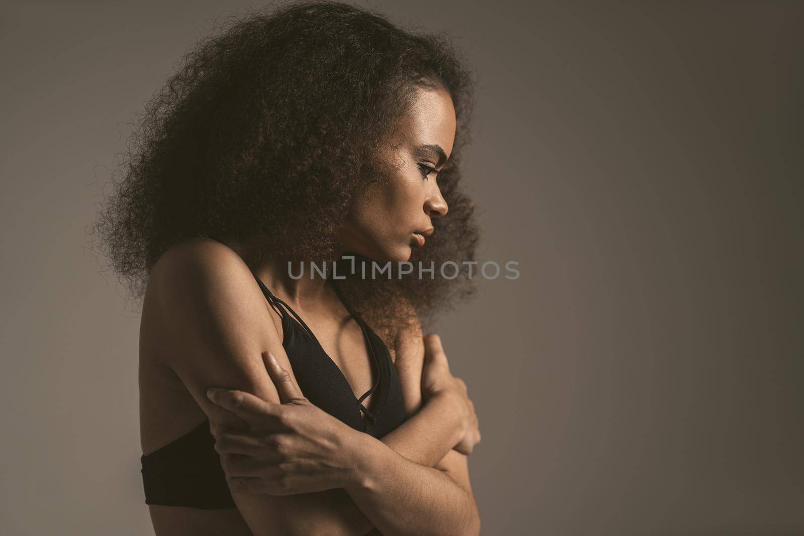 Standing sideways tender African American girl dressed in black top isolated on grey background. Human emotions, facial expression concept by LipikStockMedia