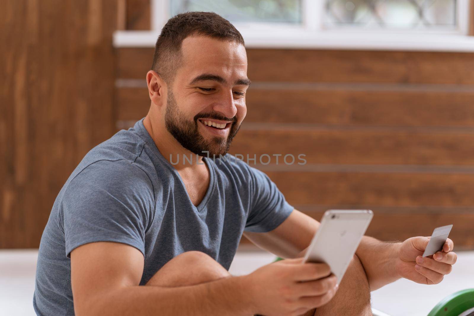 Handsome man holding smartphone doing sport bets and gambling online or buying online equipment with a debit or credit card. Sports betting apps on smartphone. Modern digital sports life by LipikStockMedia