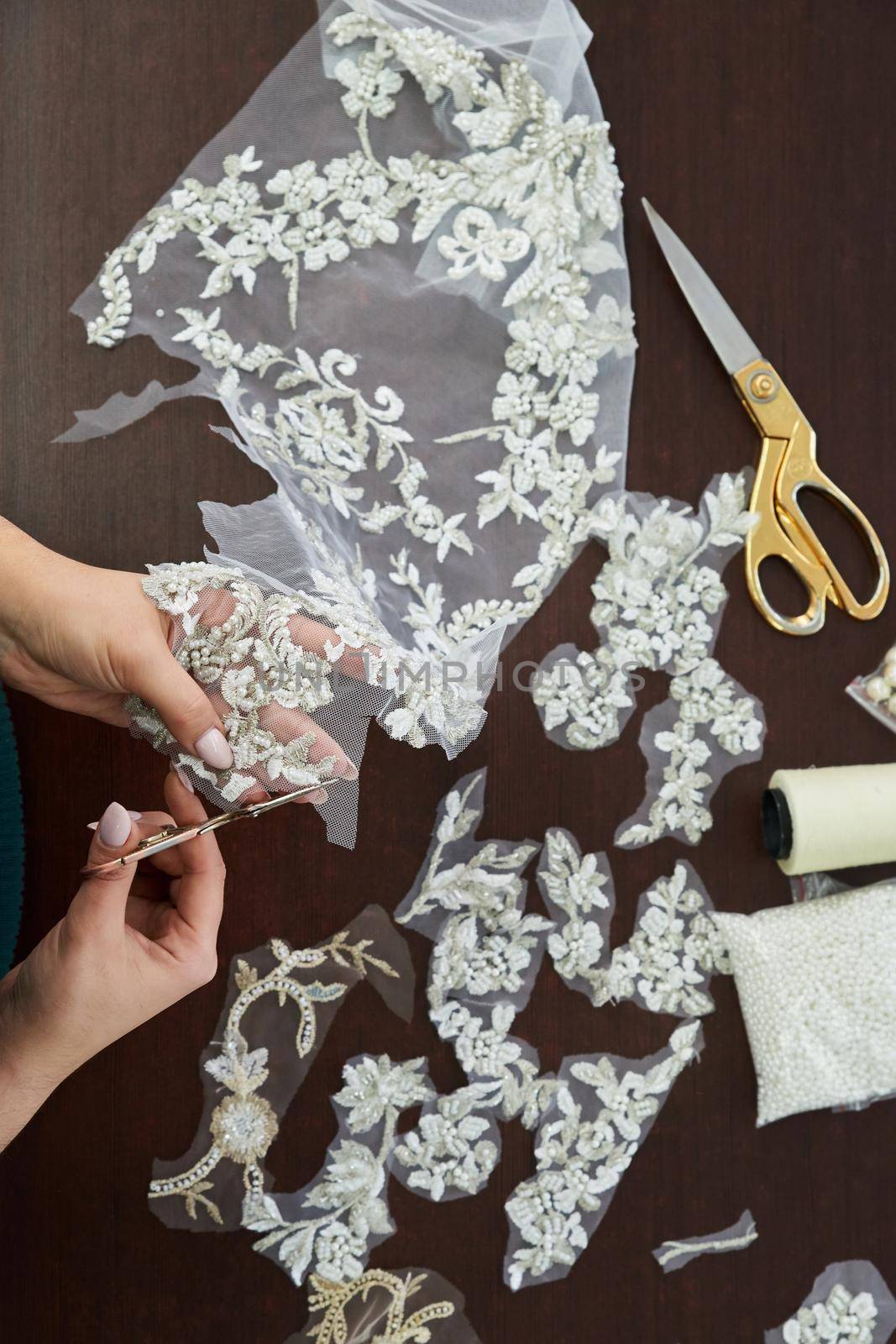 Dressmaker cutting lace fabric for wedding dress decoration by Mariakray