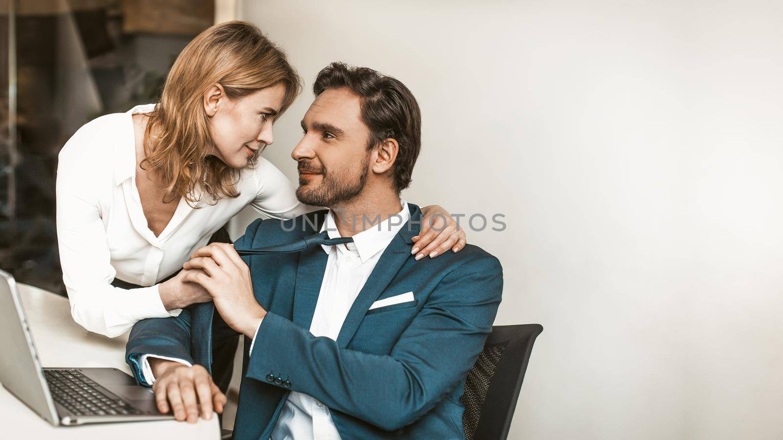 Flirting at work couple. Attractive Caucasian office workers man and woman gently look and touch each other. 16x9 format. Template for banner with empty place or copy space at right side by LipikStockMedia