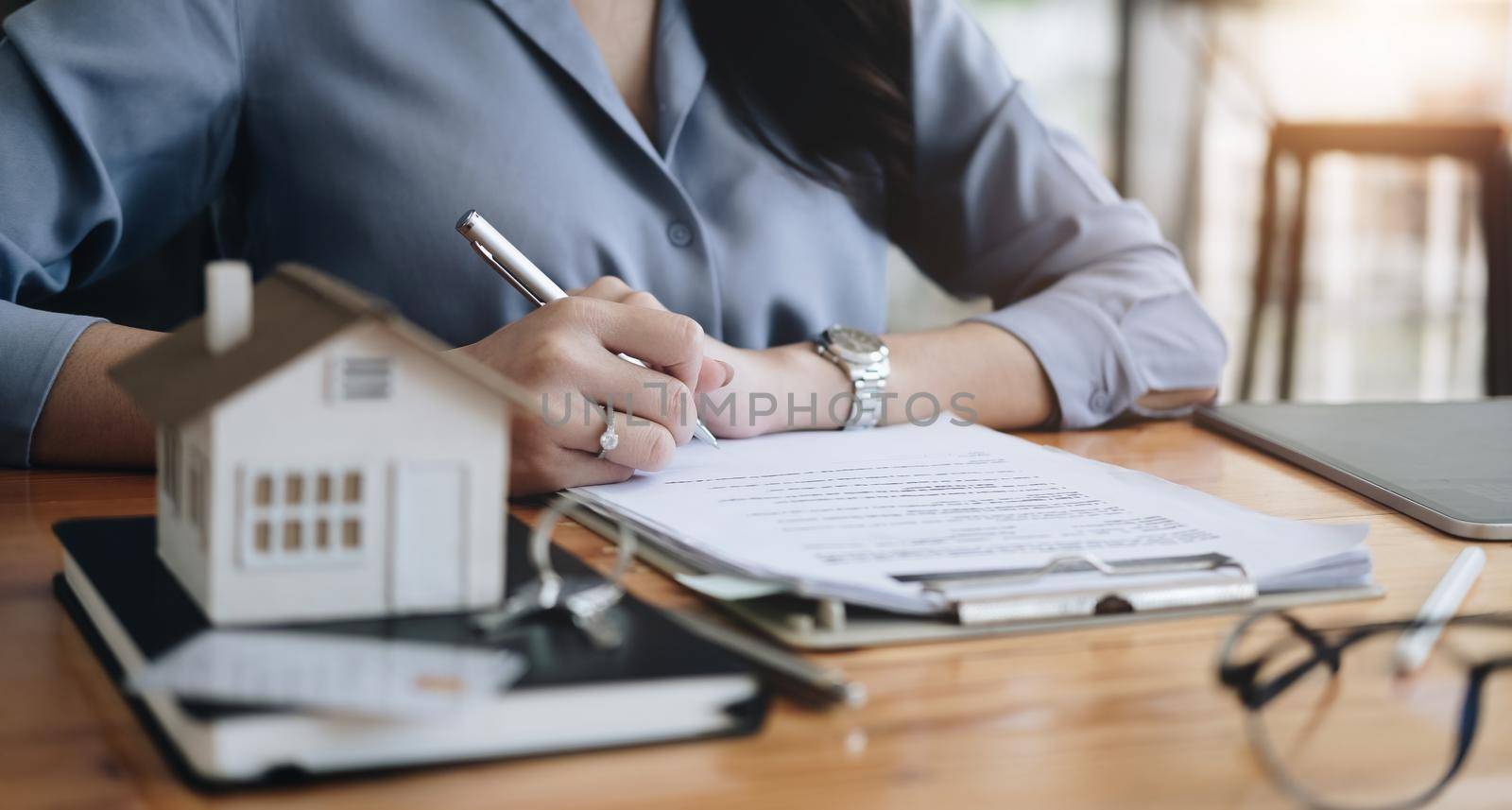 Real estate agent working sign agreement document contract for home loan insurance approving purchases for client with house model and key on wooden desk.