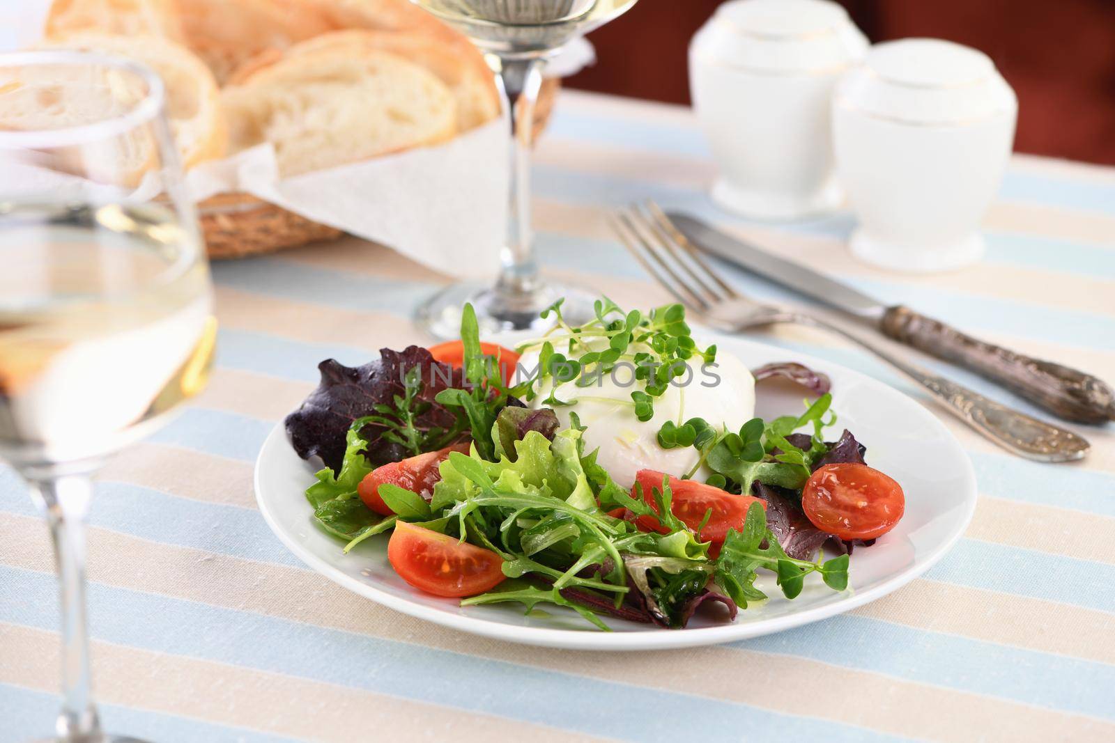 A healthy salad made from a lettuce leaves vegetables mix greens portion, arugula, tomatoes, radish sprouts and mozzarella cheese, olive oil and fresh bread, and a glass of white wine

