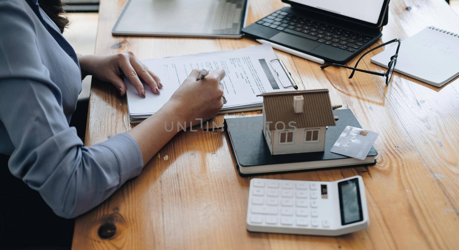 Real estate agent working sign agreement document contract for home loan insurance approving purchases for client with house model and key on wooden desk.