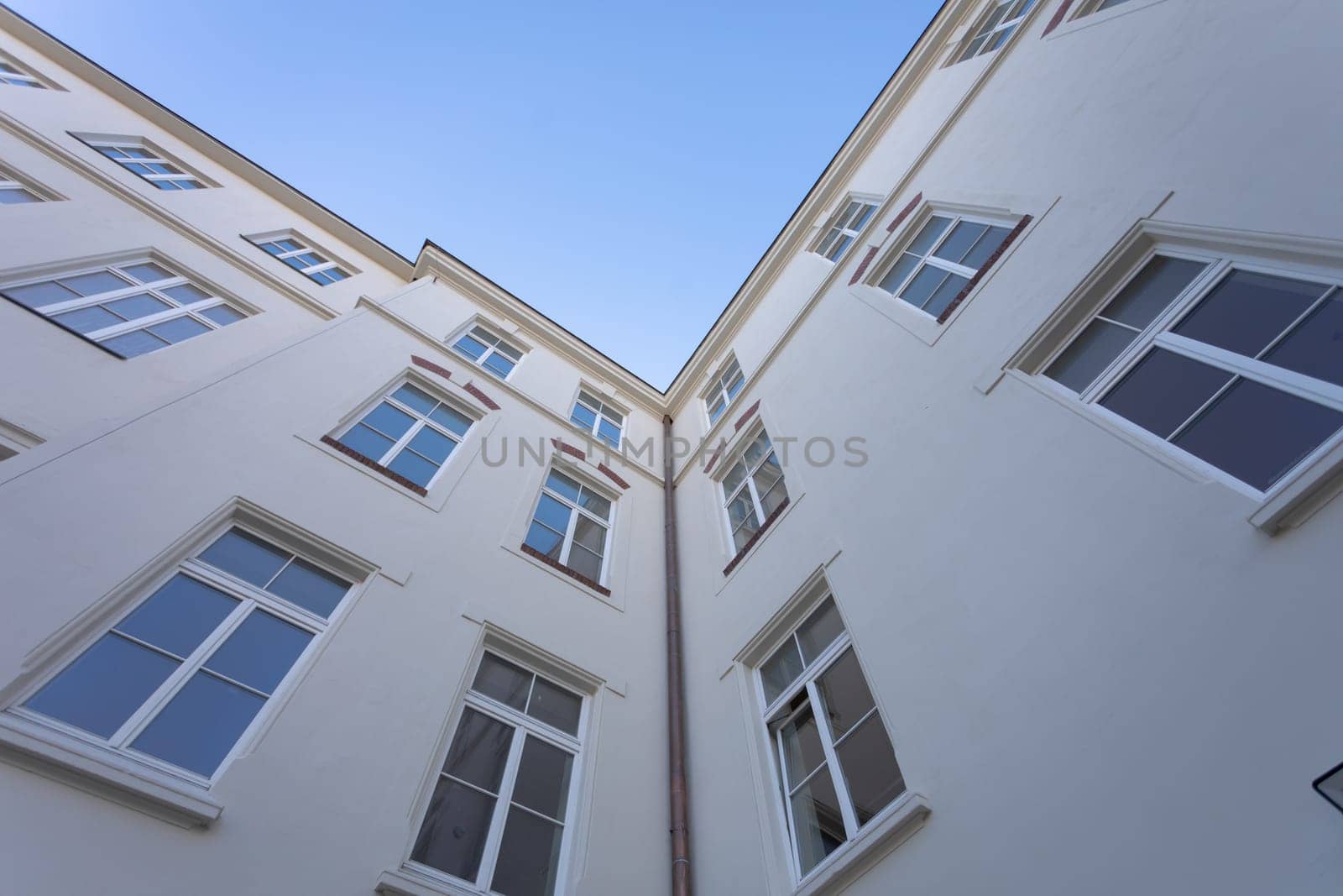 The walls of the building as seen from a lower perspective. A row of multiple windows in the curtain wall of a tall building. Clear blue sky.