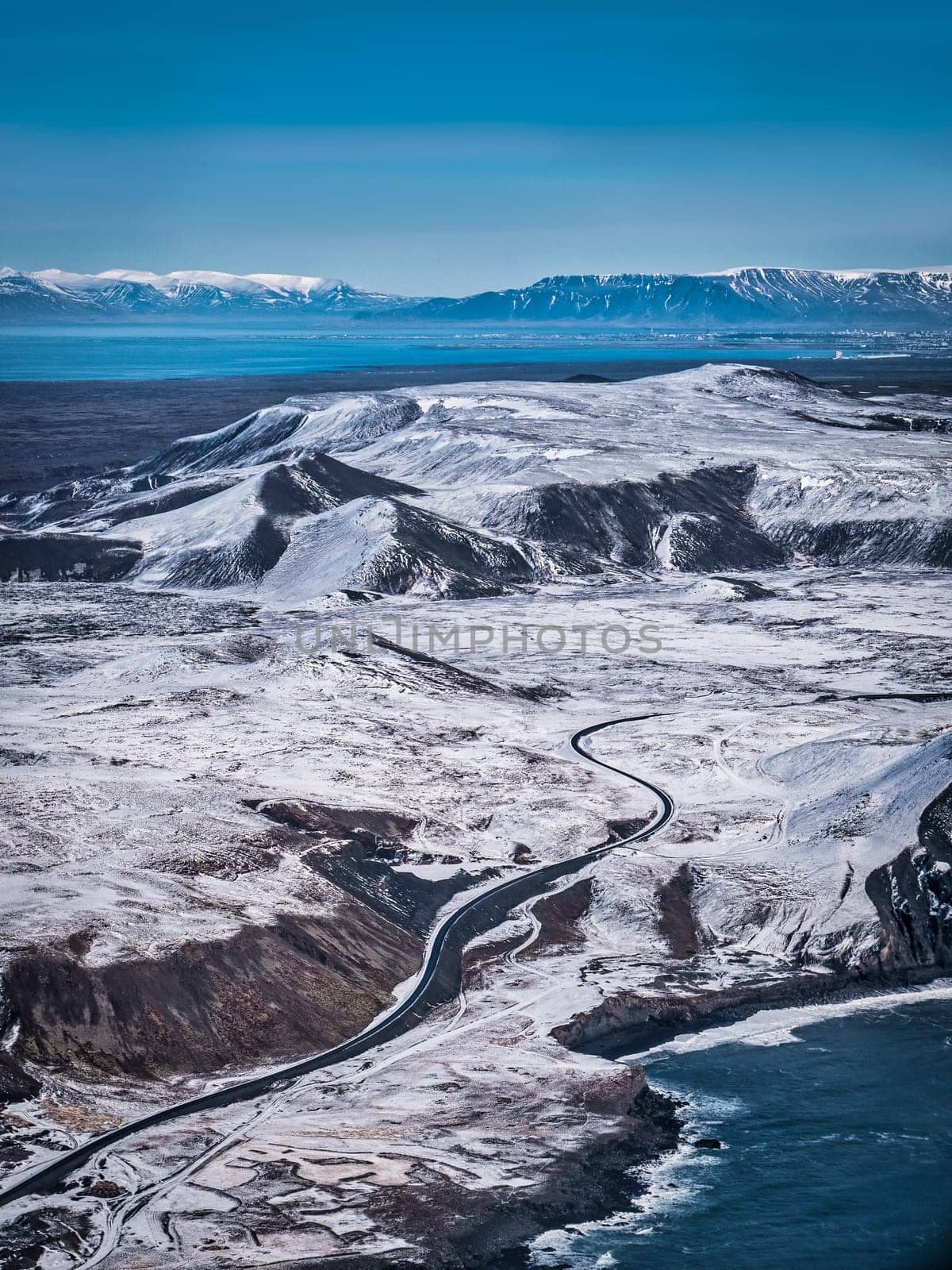 Drone view of majestic scenery with snowy mountains washed by wavy ocean on sunny day