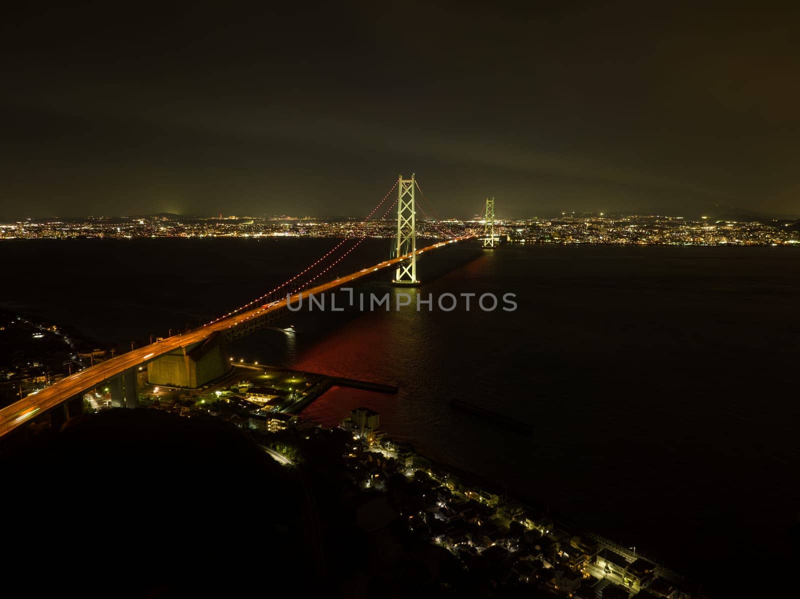 Akashi Kaikyo suspension bridge over dark water between city lights at night. High quality photo