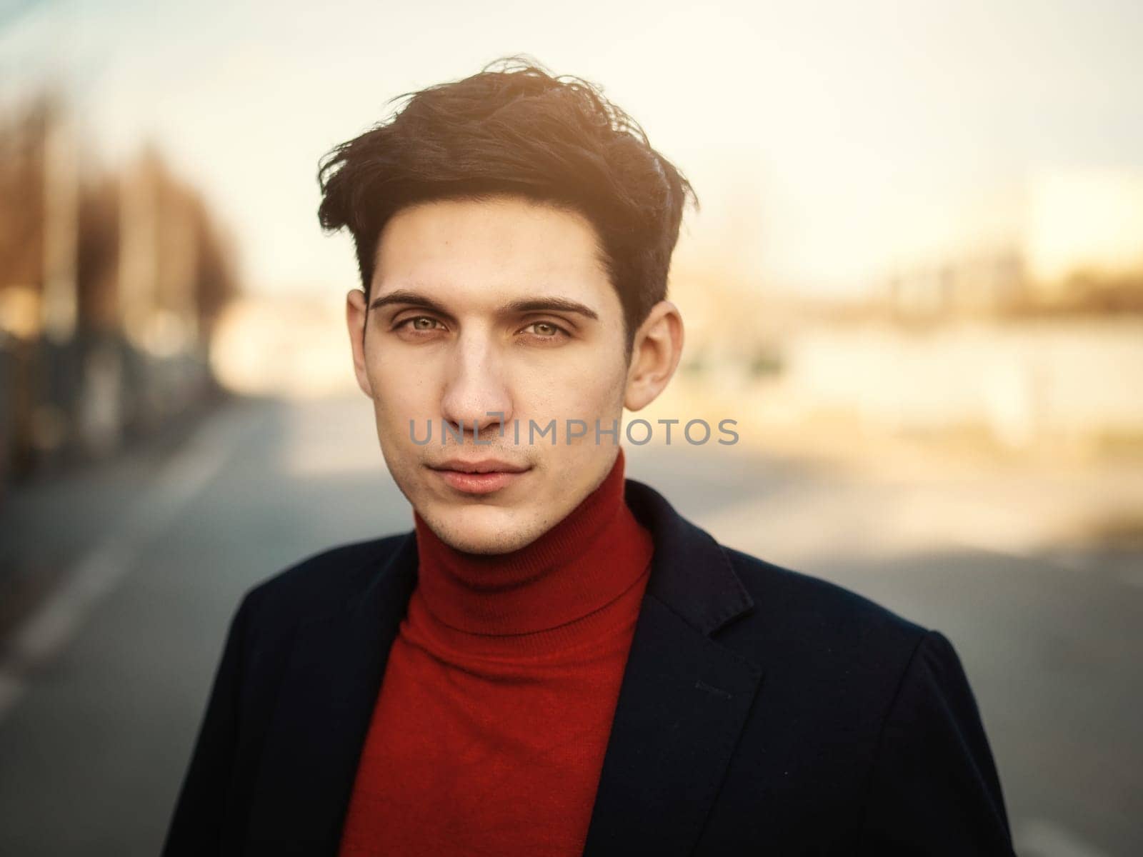 Handsome young man in city street, looking at camera with serious expression, wearing suit jacket and turtleneck