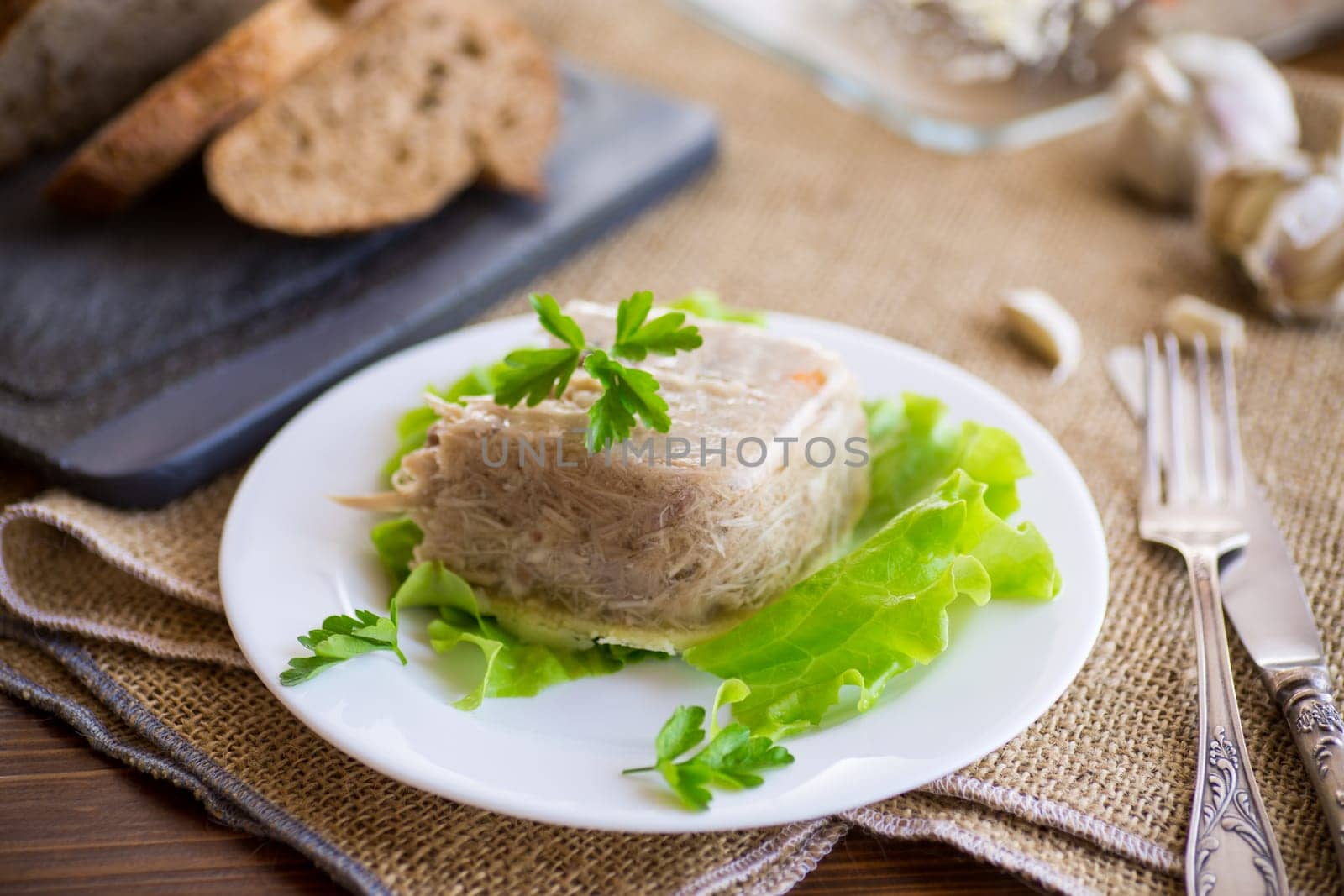 Boiled chicken meat aspic in meat gelatin broth in a plate on a wooden table