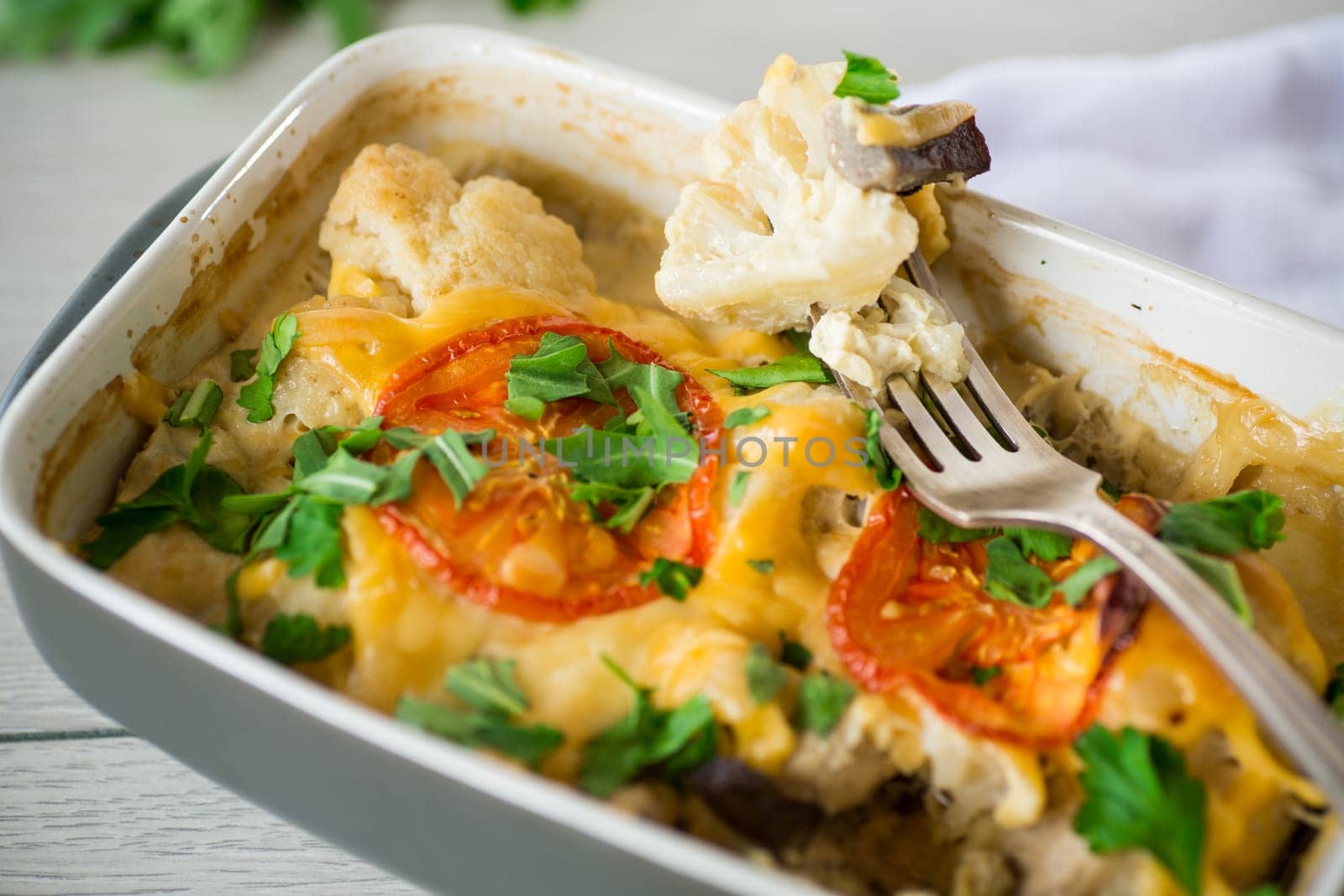 cauliflower baked with chicken fillet and mushrooms under cheese in a ceramic form, on a wooden table.