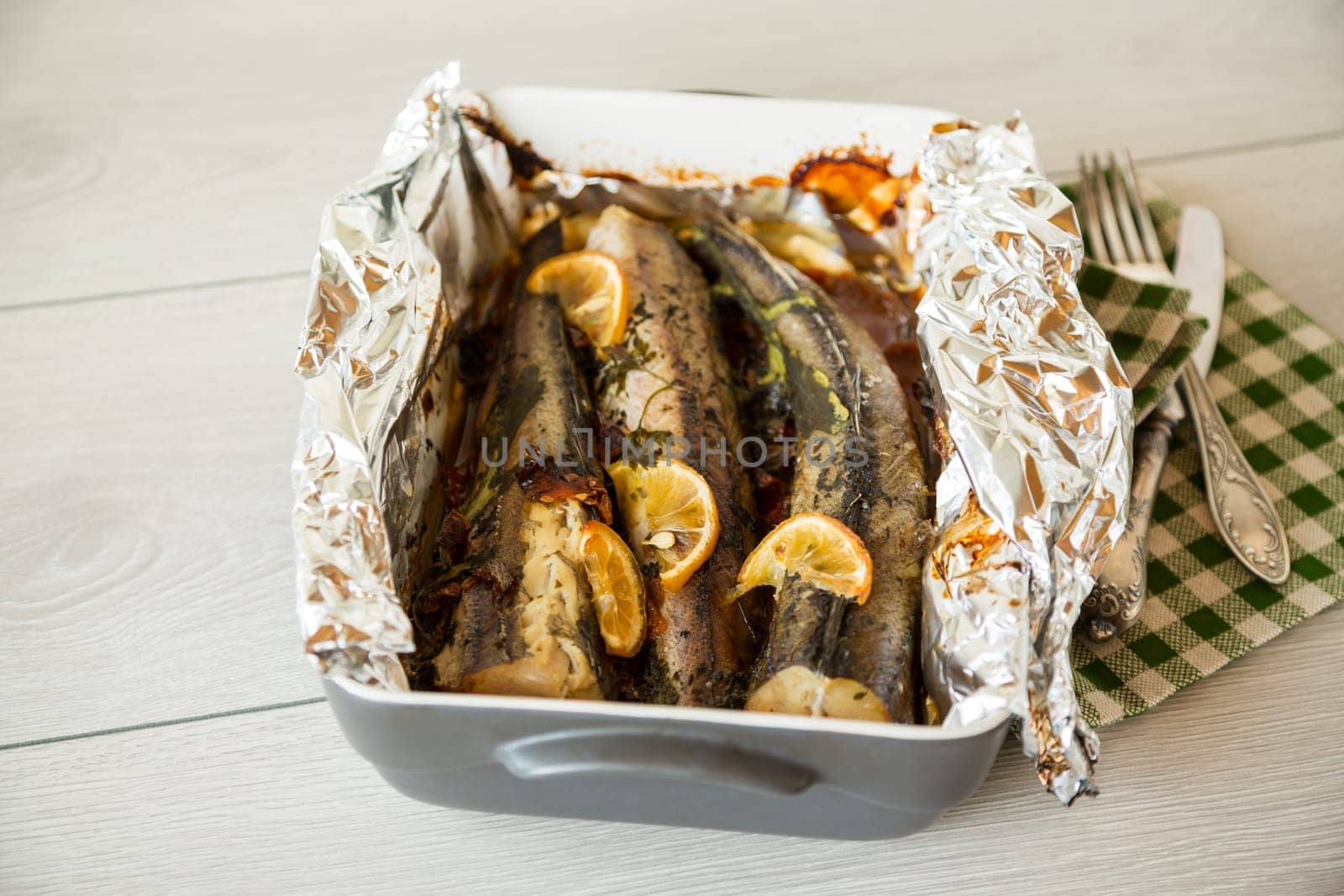 Baked fish with seasonings and spices in foil, in a ceramic form.