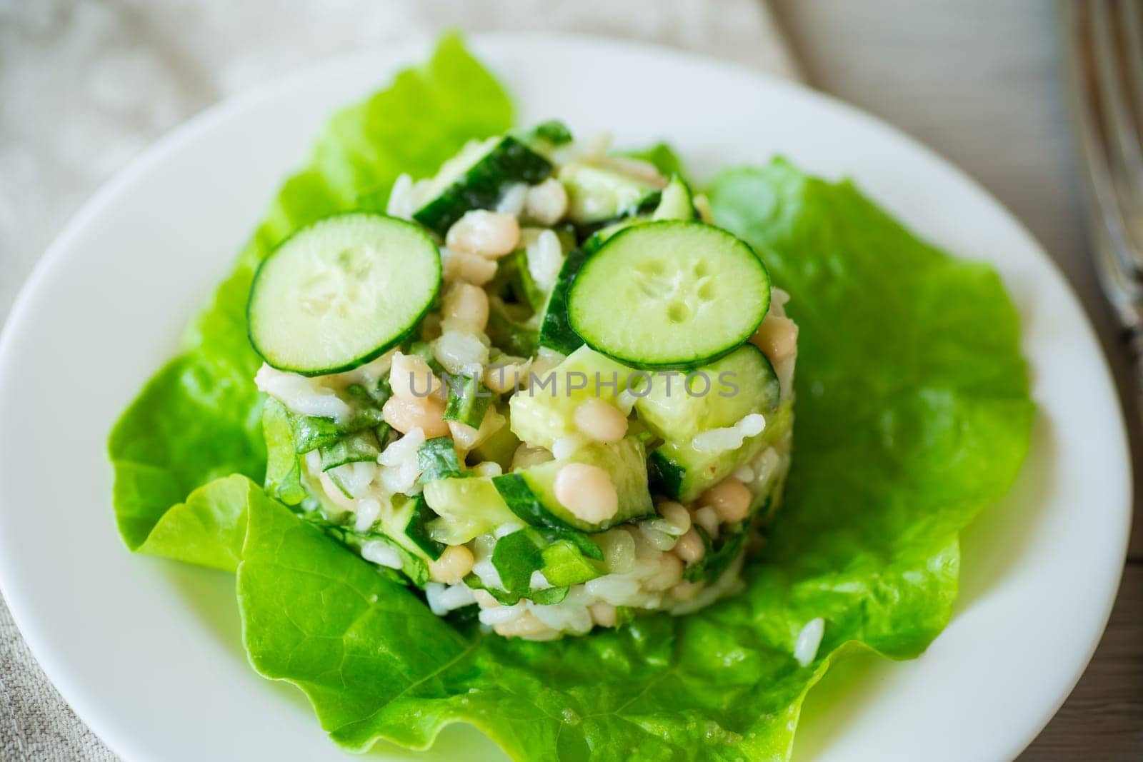 fresh summer salad with beans, rice, cucumbers and other vegetables in a plate on a wooden table.