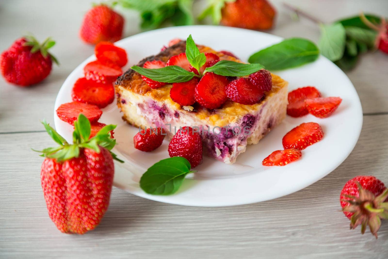 cooked cottage cheese casserole with berry and strawberry filling in a plate on the table