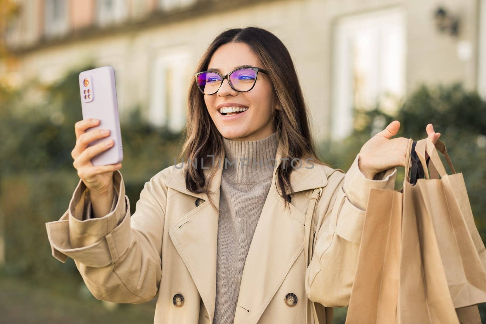 Easy shopping. Beautiful fashionable woman holding a phone and ecological paper bags in the street.