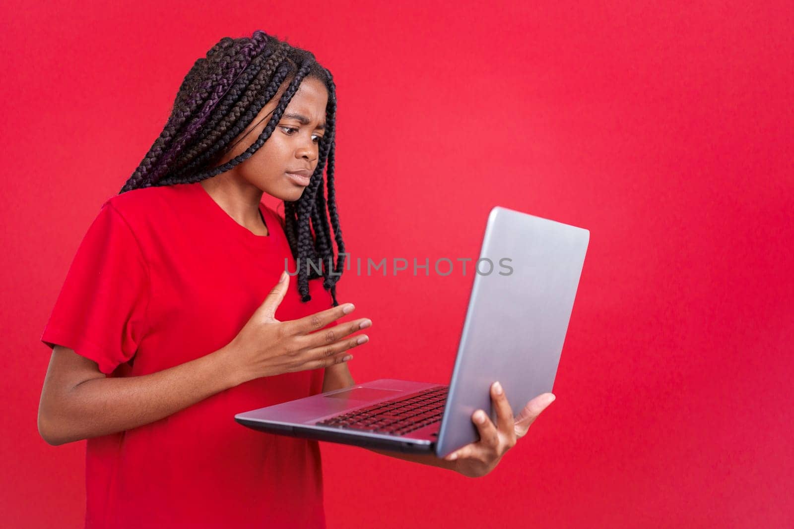 African woman having a problem with a laptop in studio with red background